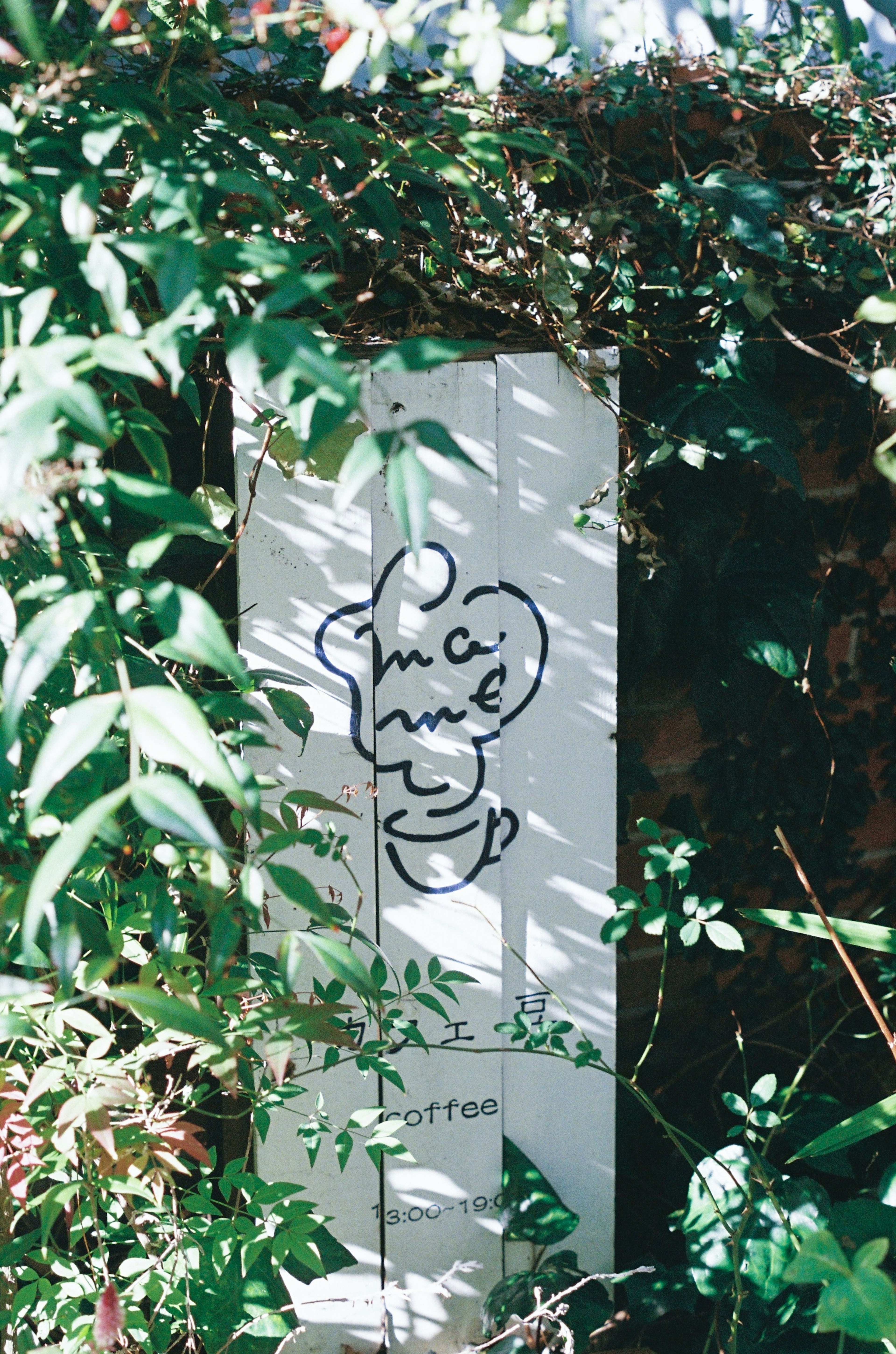 A white sign surrounded by green plants featuring a simple character illustration