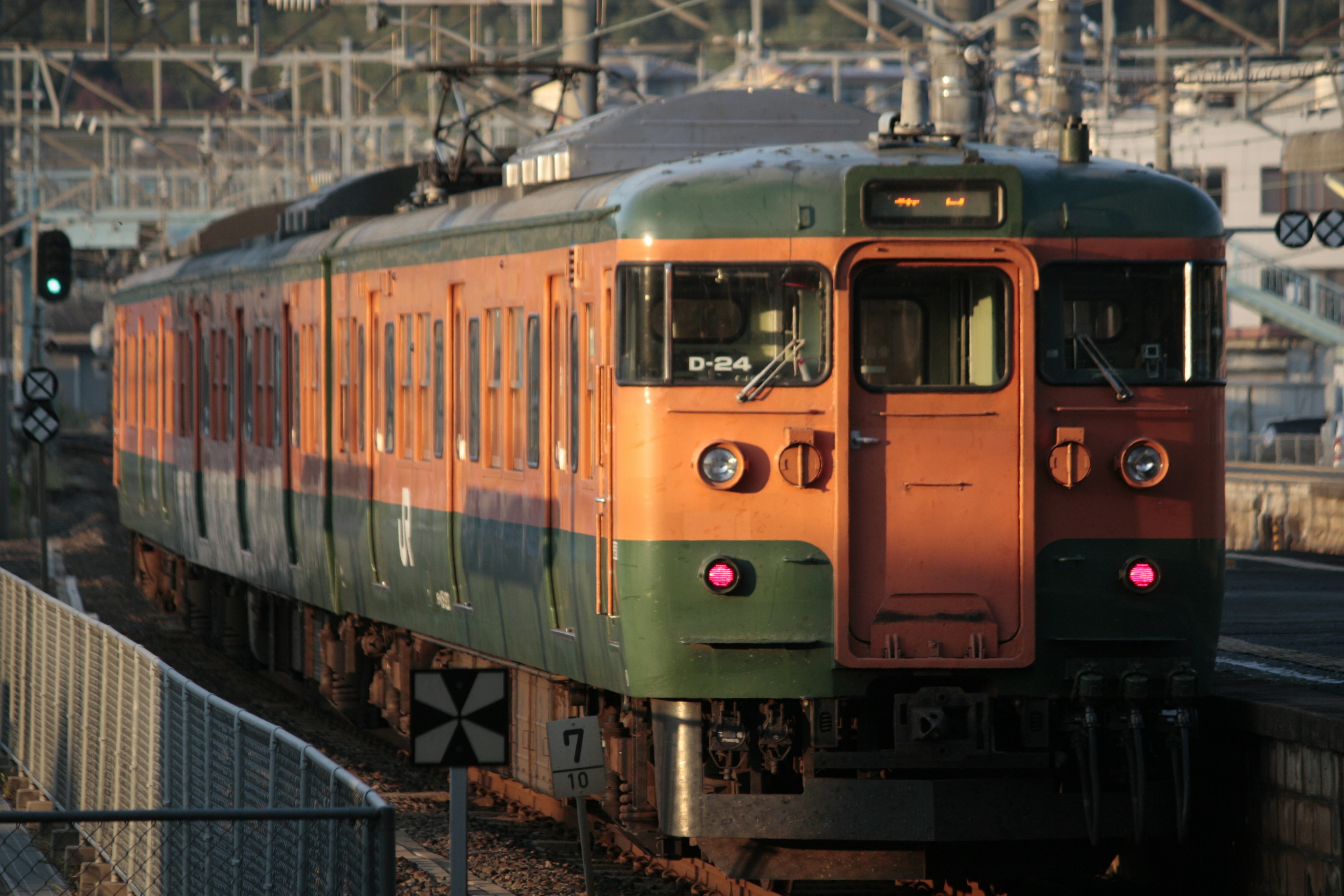 橙色和綠色的火車在日落時停靠在車站