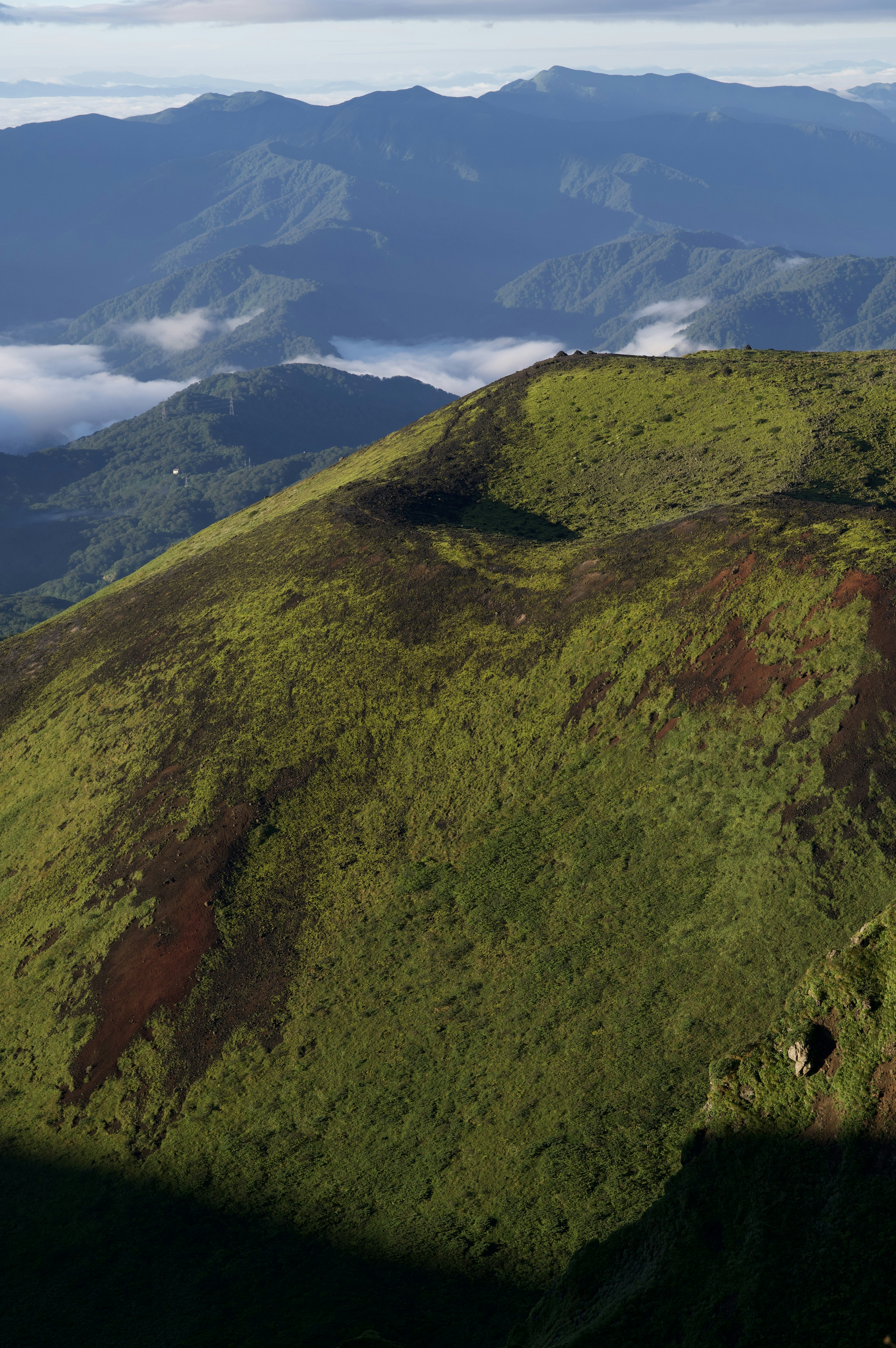 Lush green mountain ridge with distant peaks and clouds