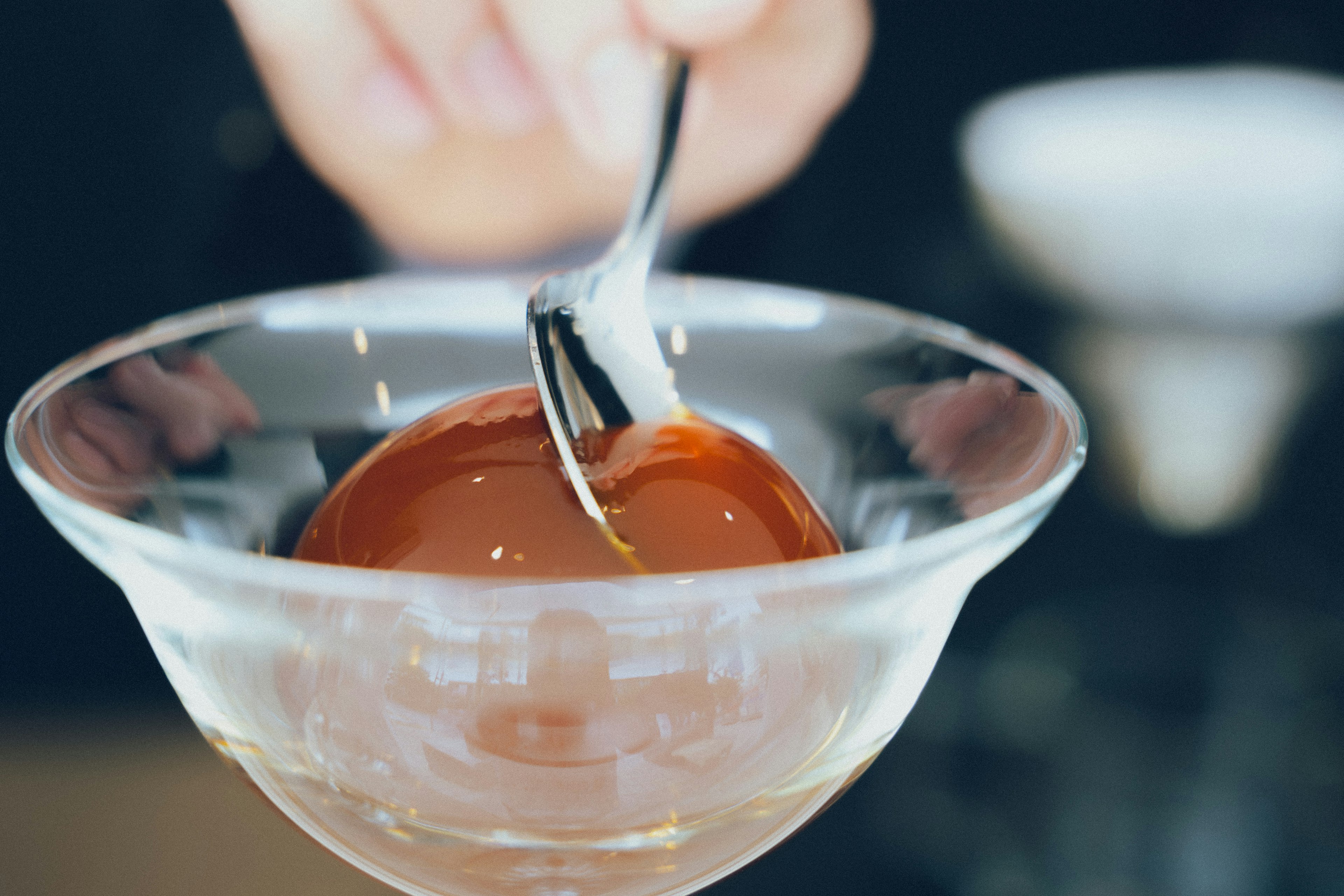 Una mano sacando un postre gelatinoso de un bol de vidrio transparente con una cuchara