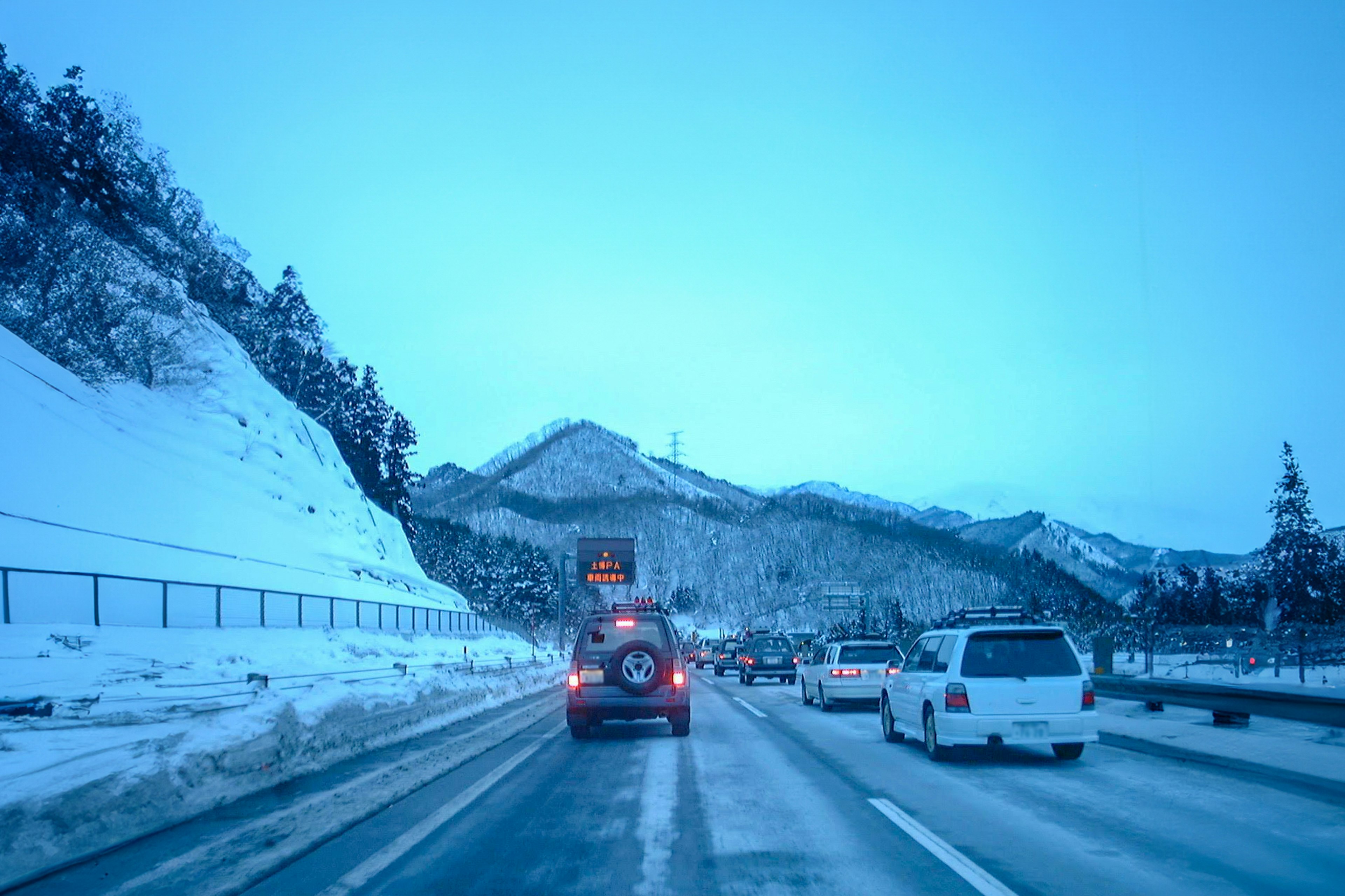 Coches conduciendo por una carretera de montaña nevada con cielo azul