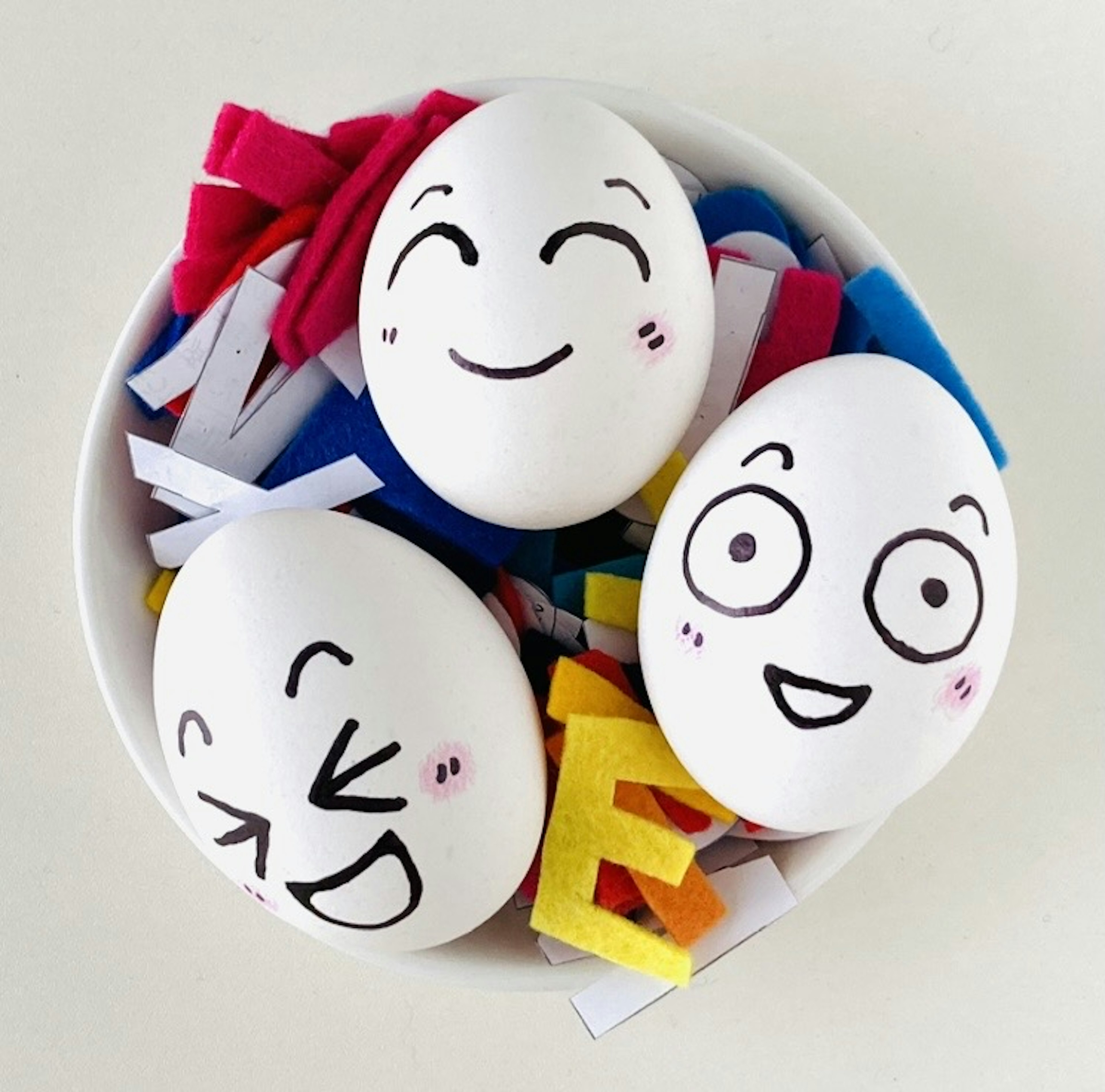 A bowl filled with colorful paper scraps featuring white eggs with drawn smiling faces