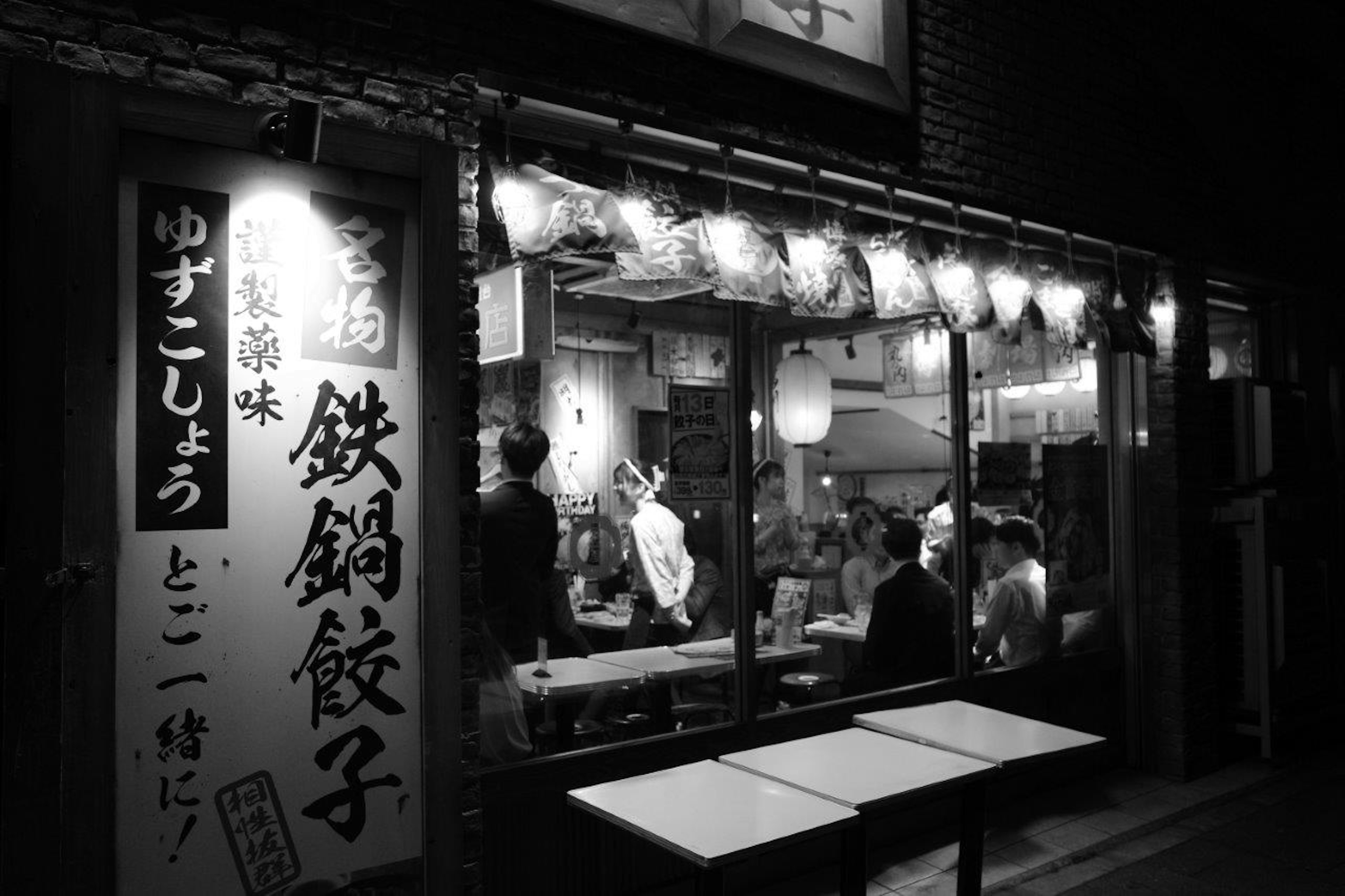 夜の街にある賑やかな餃子店の外観 明るい提灯と人々が映る