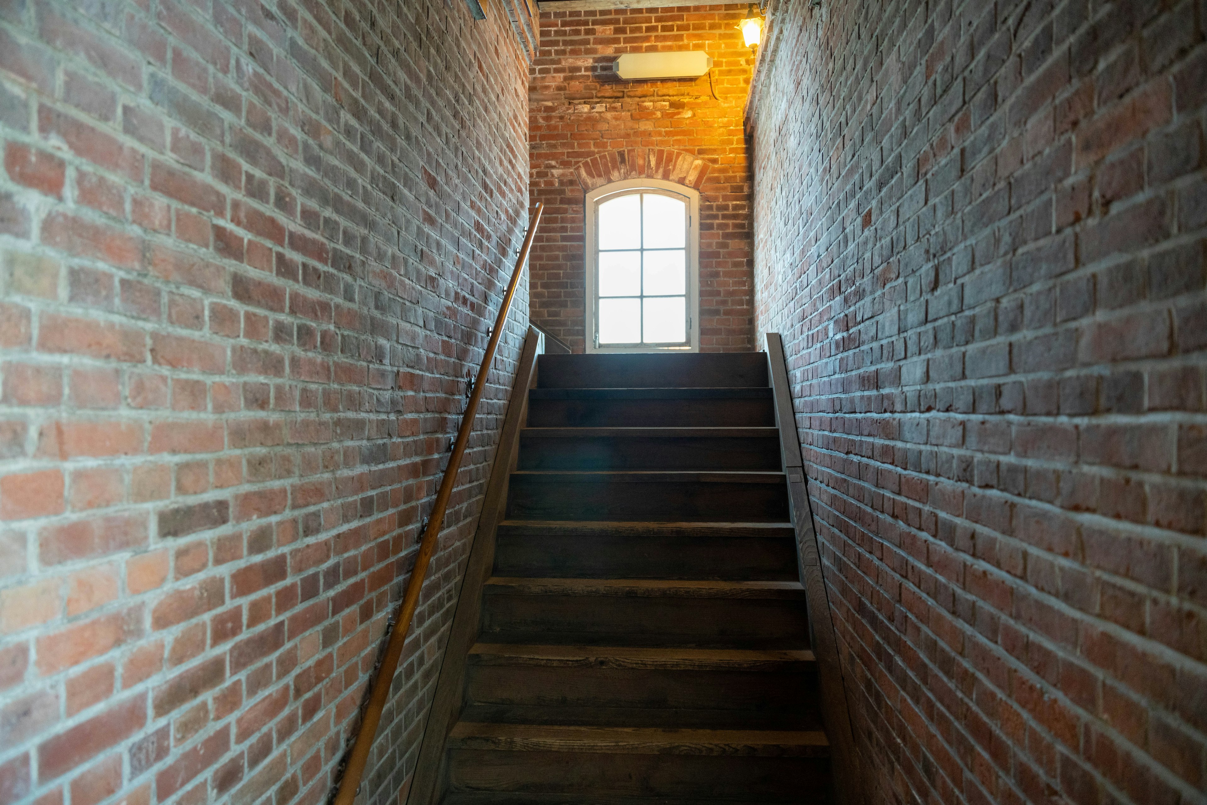 Narrow passage with brick walls leading up a staircase to a window