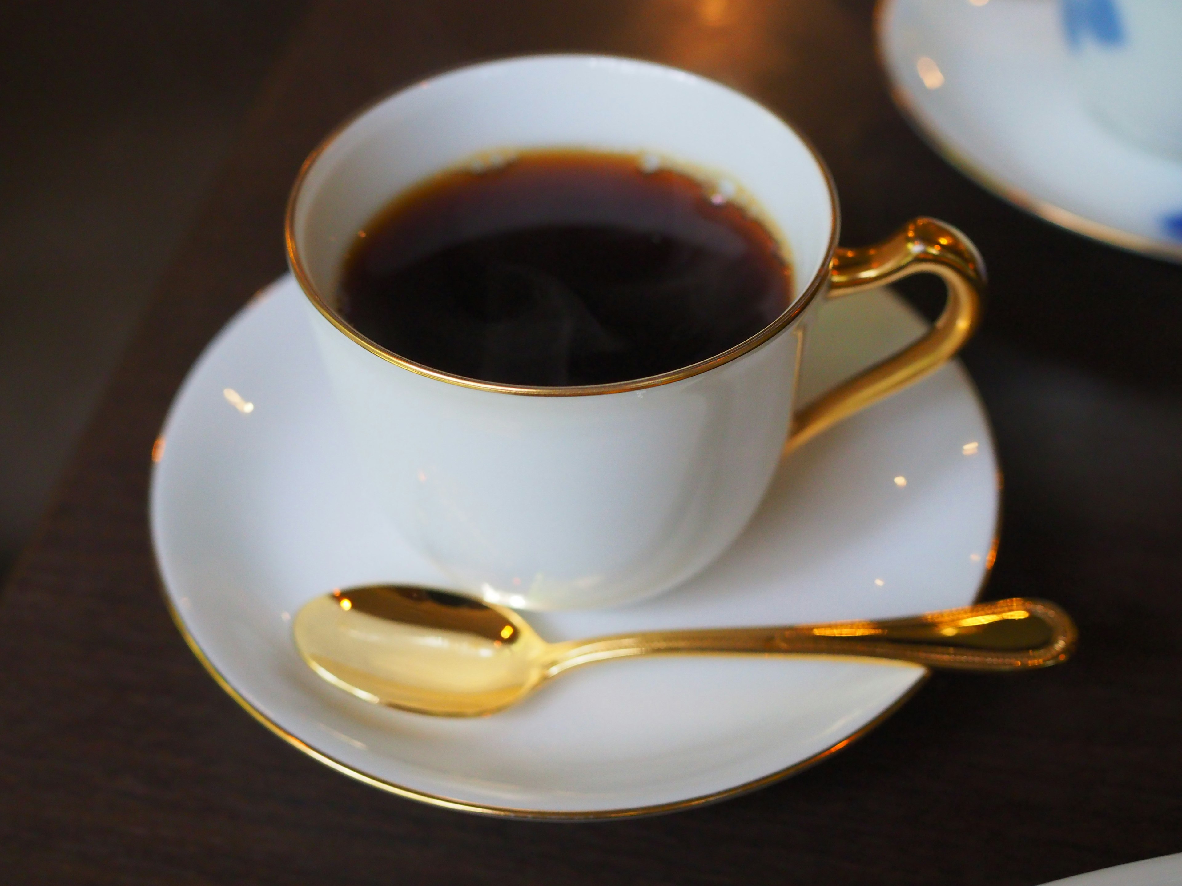 Café en una taza blanca con una cuchara dorada en un platillo