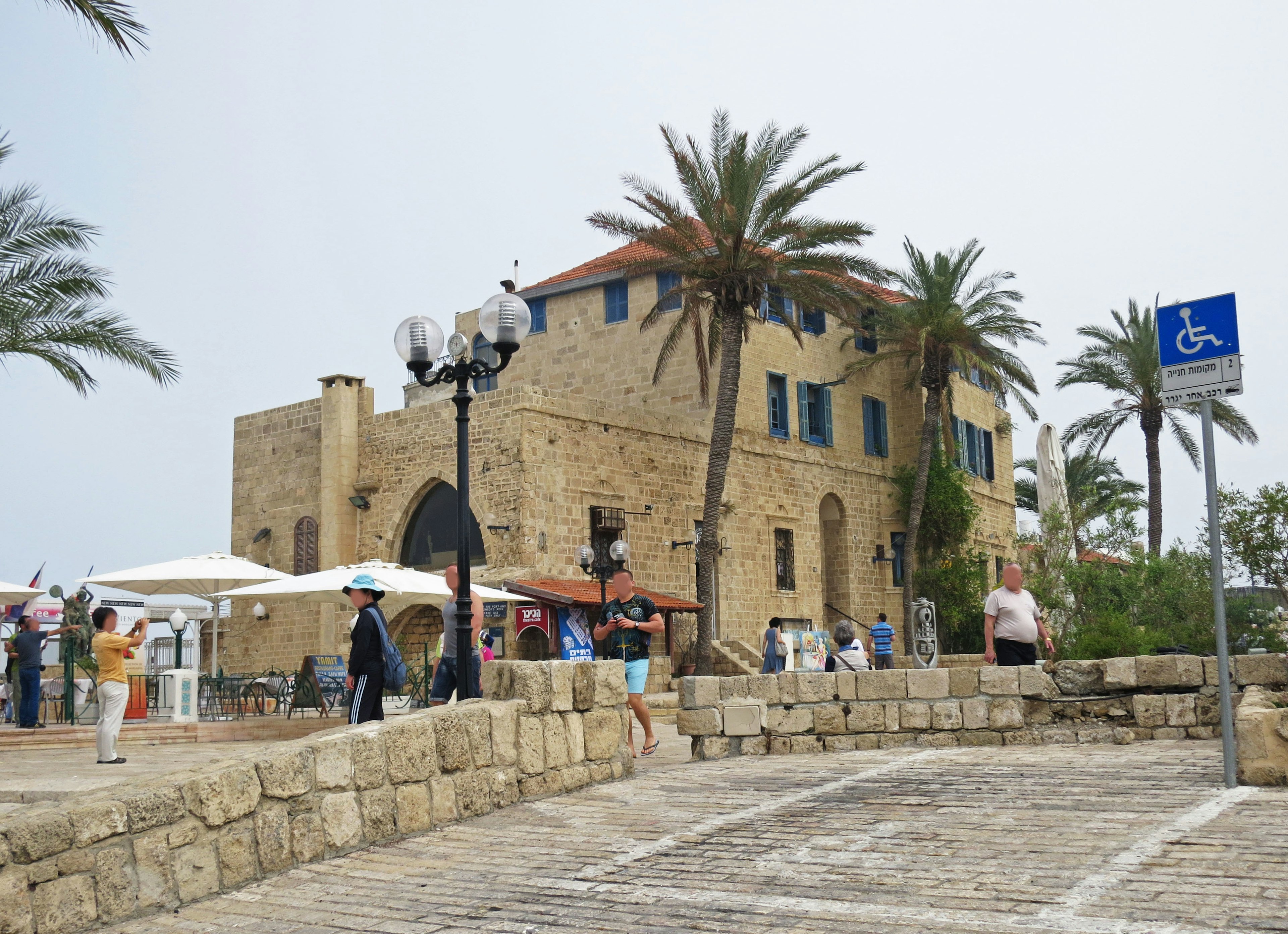 Historic stone building with palm trees and people gathering