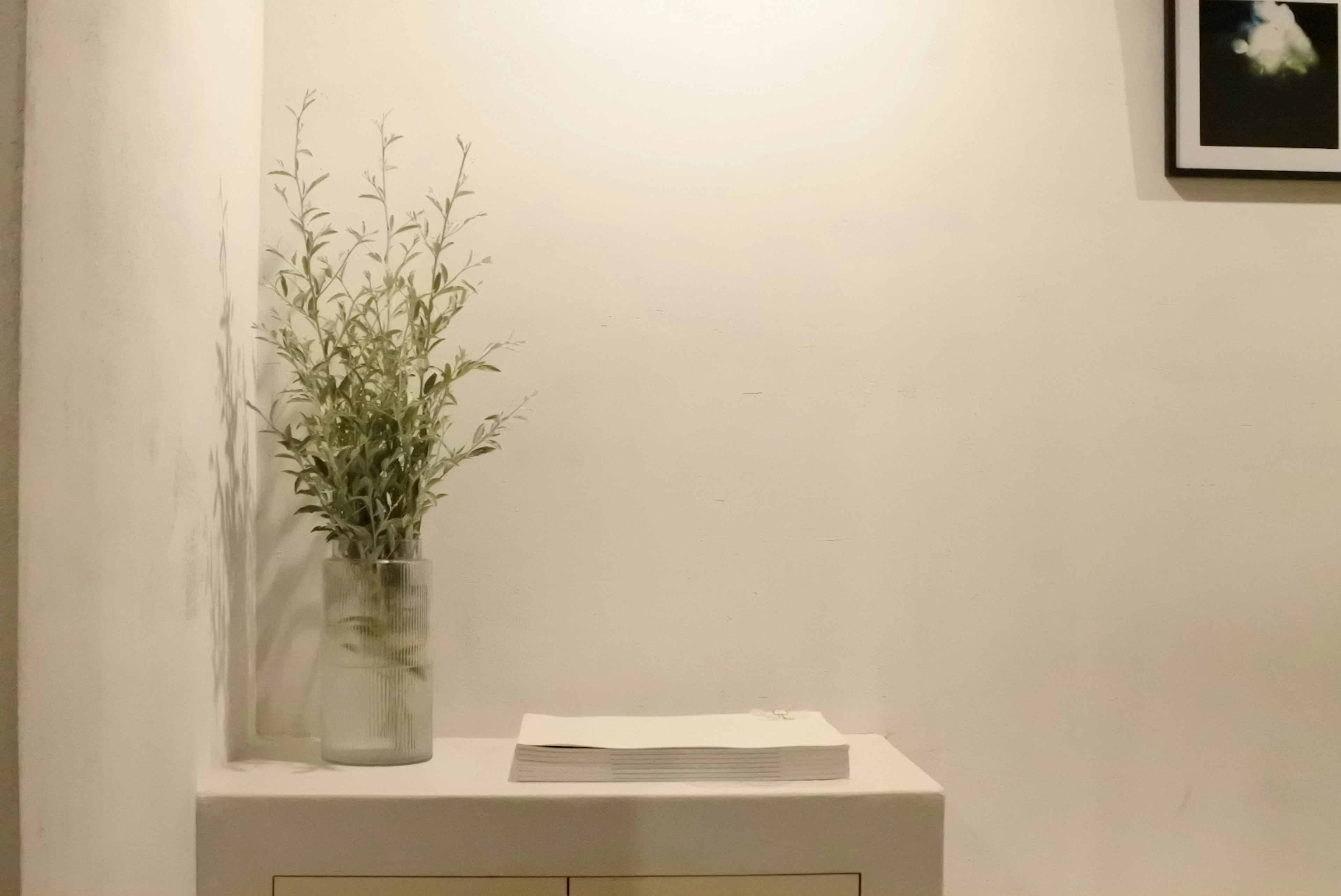 Un vase blanc avec de la verdure sur une table blanche contre un mur blanc