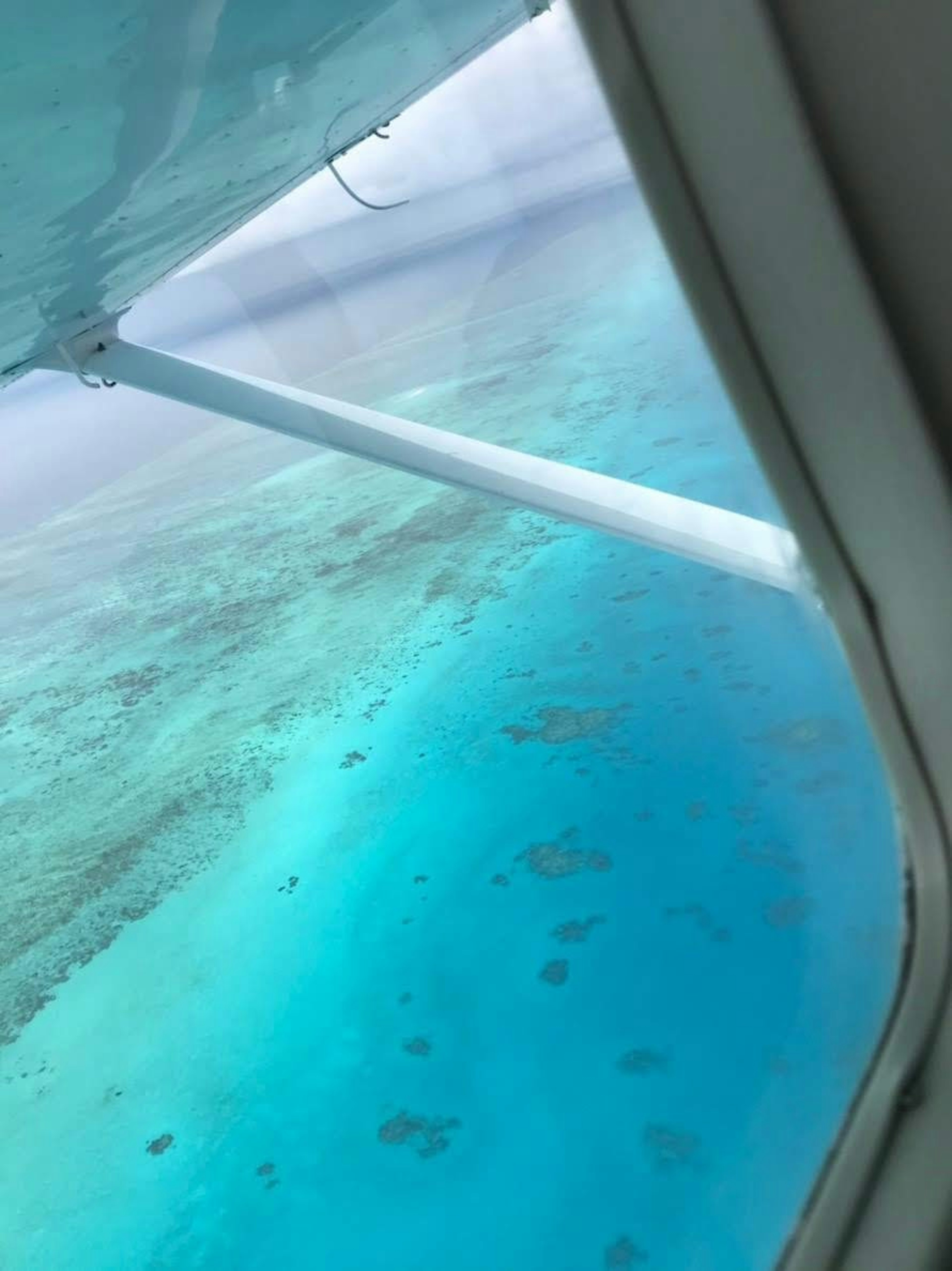 Pemandangan laut turquoise dan terumbu karang dari jendela pesawat