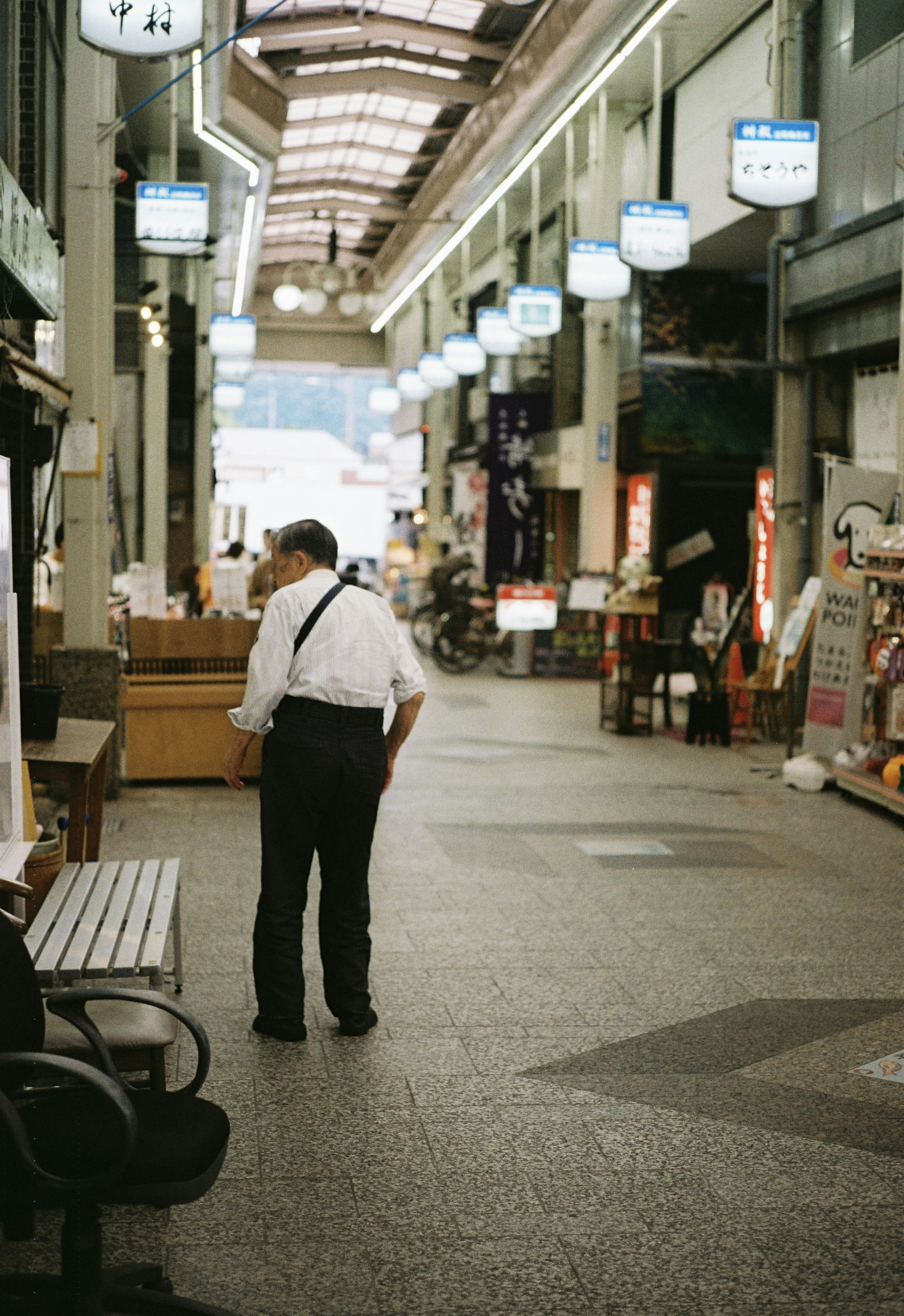 Un hombre con camisa blanca y pantalones negros caminando en una tranquila arcade comercial