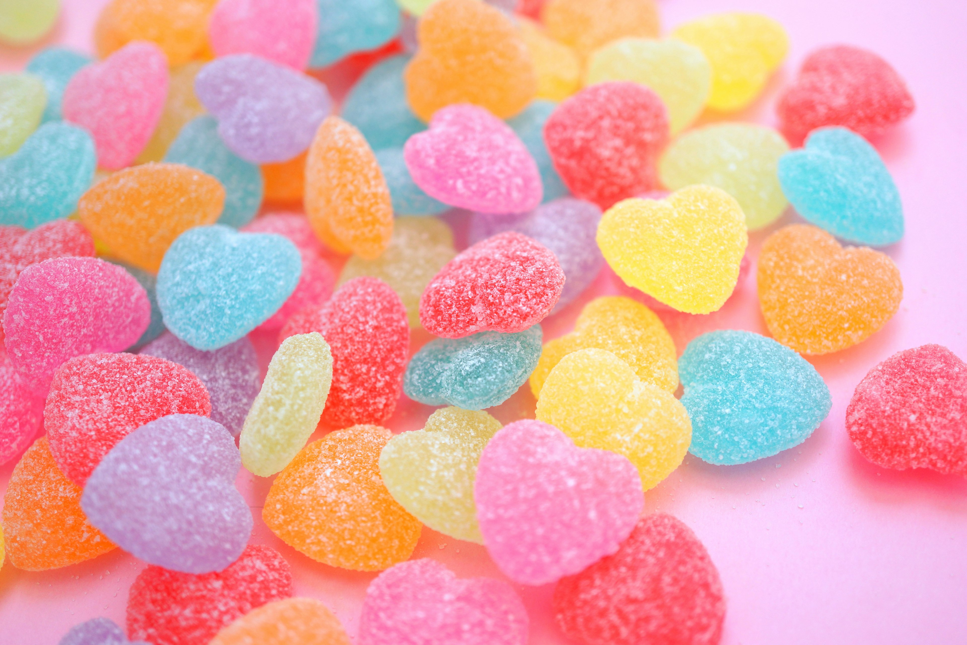 Colorful heart-shaped gummy candies scattered on a pink background