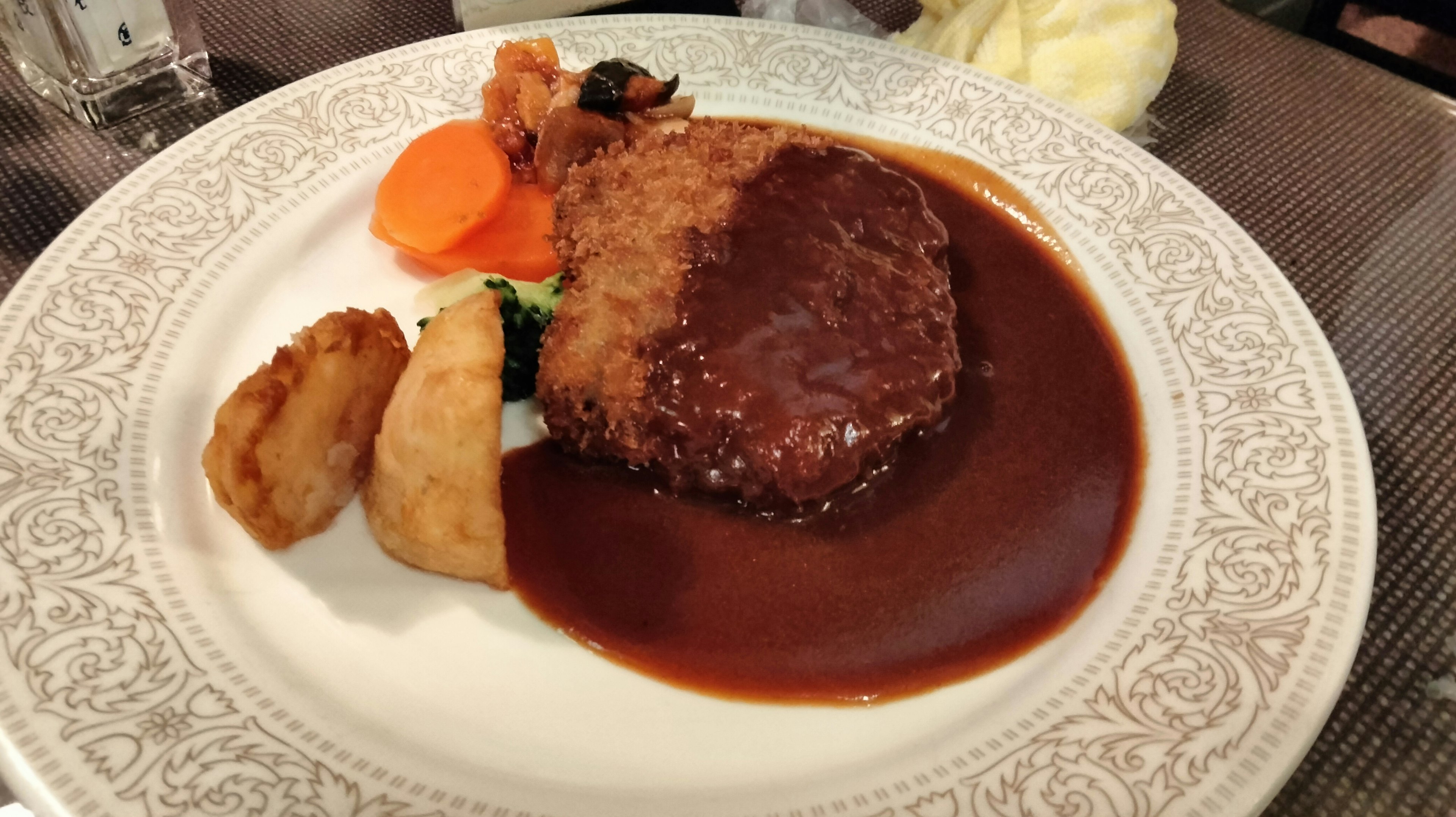 Fried chicken topped with demi-glace sauce served with carrots and potato on a decorative plate