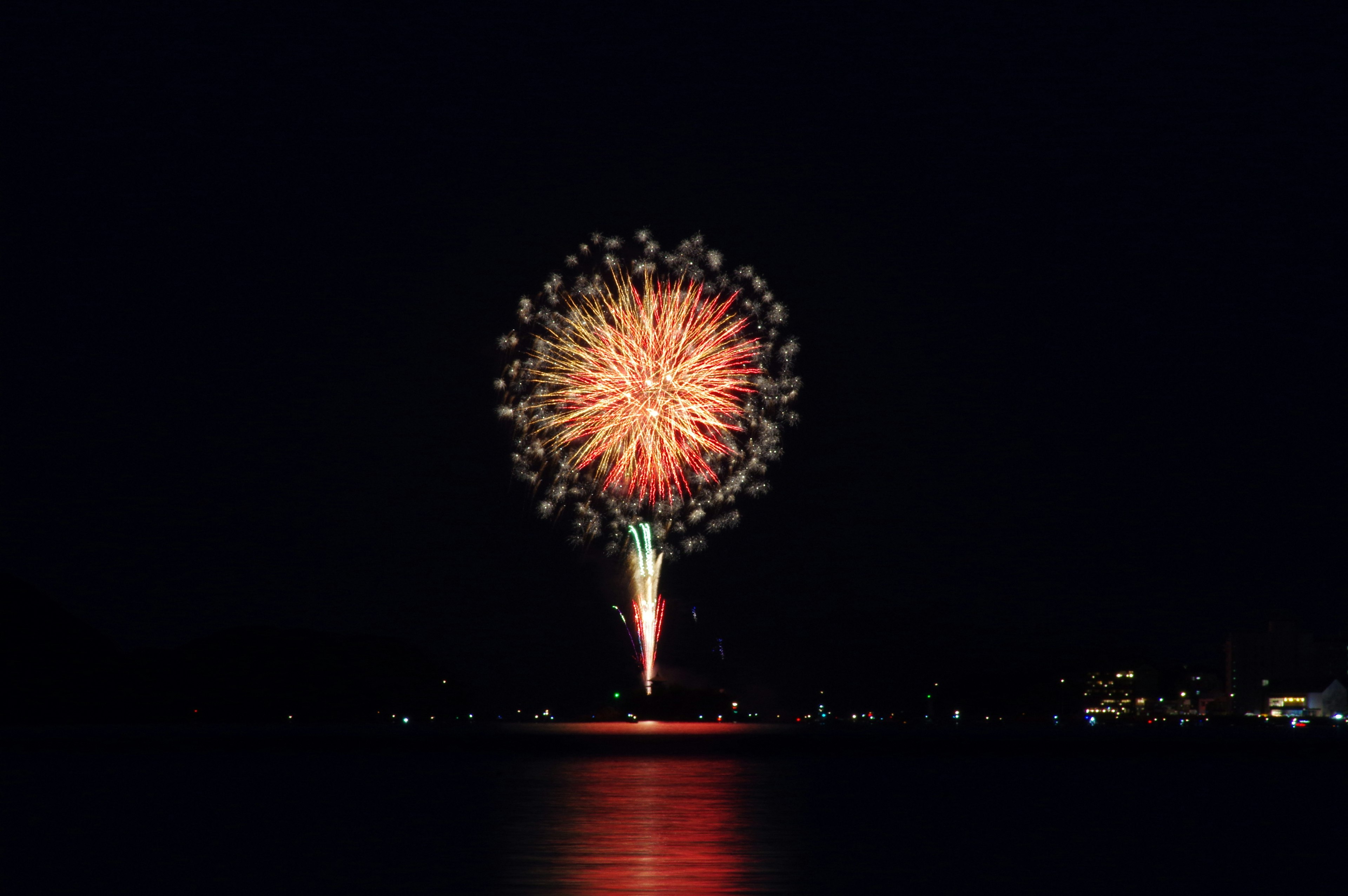 A large firework blooming in the night sky reflecting on the water