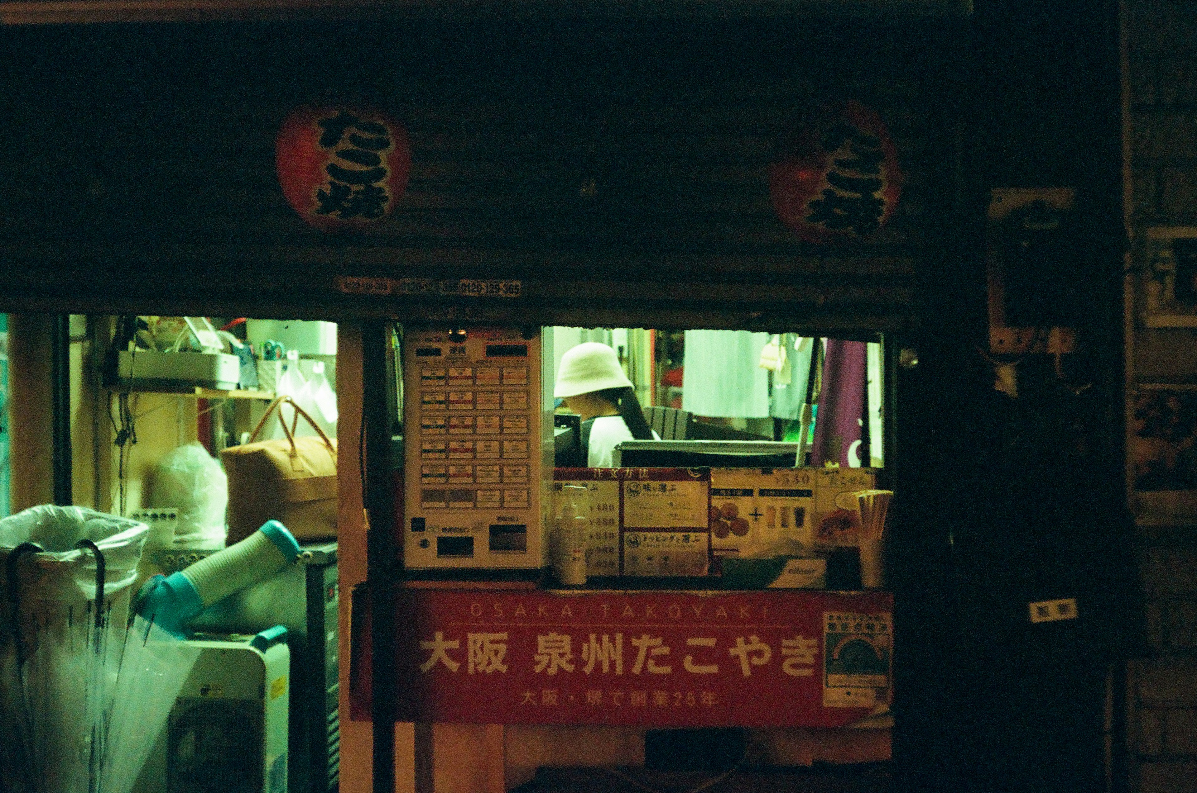 Vista nocturna de una tienda de takoyaki en Osaka con iluminación verde visible a través de la ventana