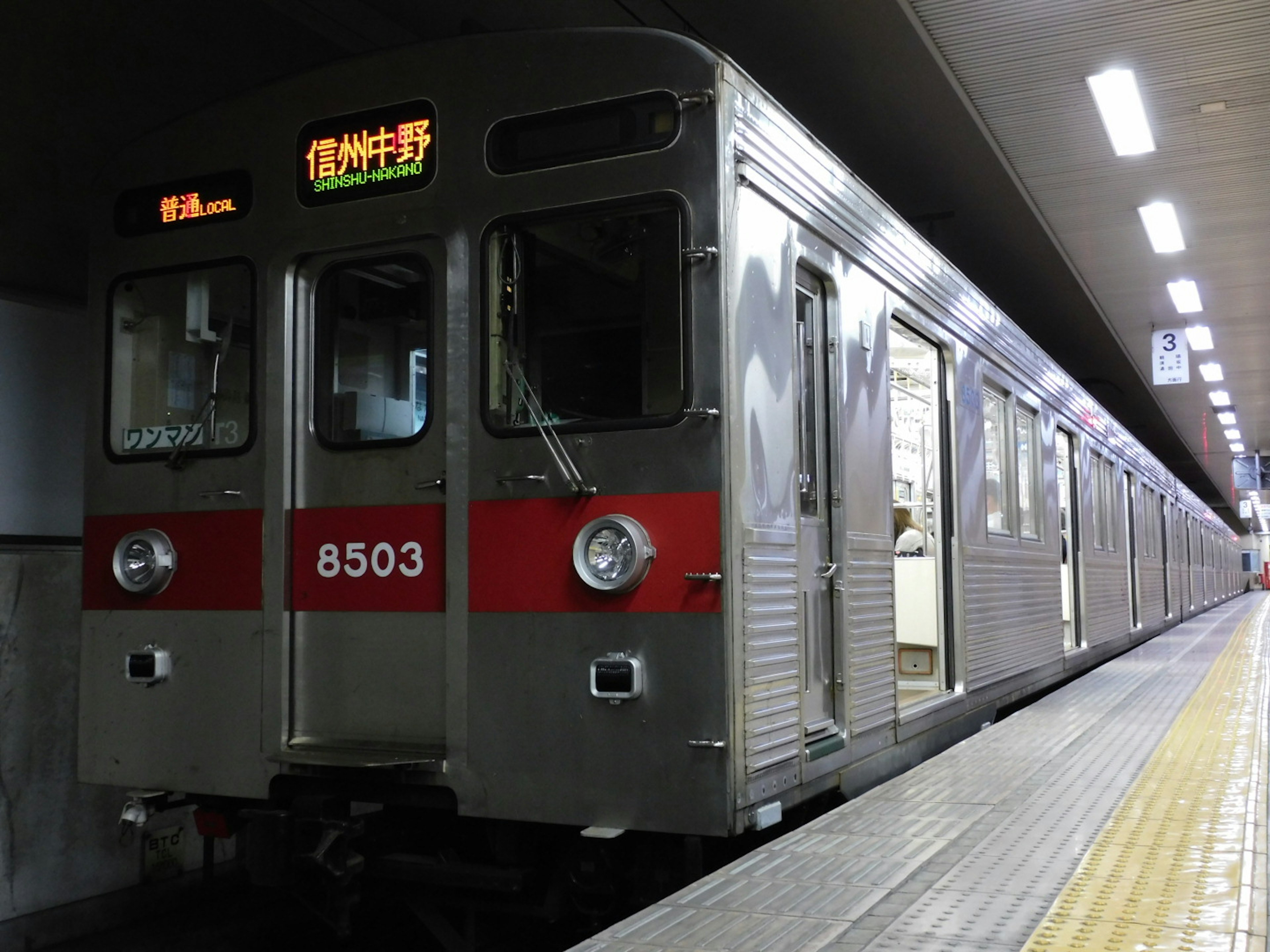 Silver subway train stopped at the station displaying number 8503