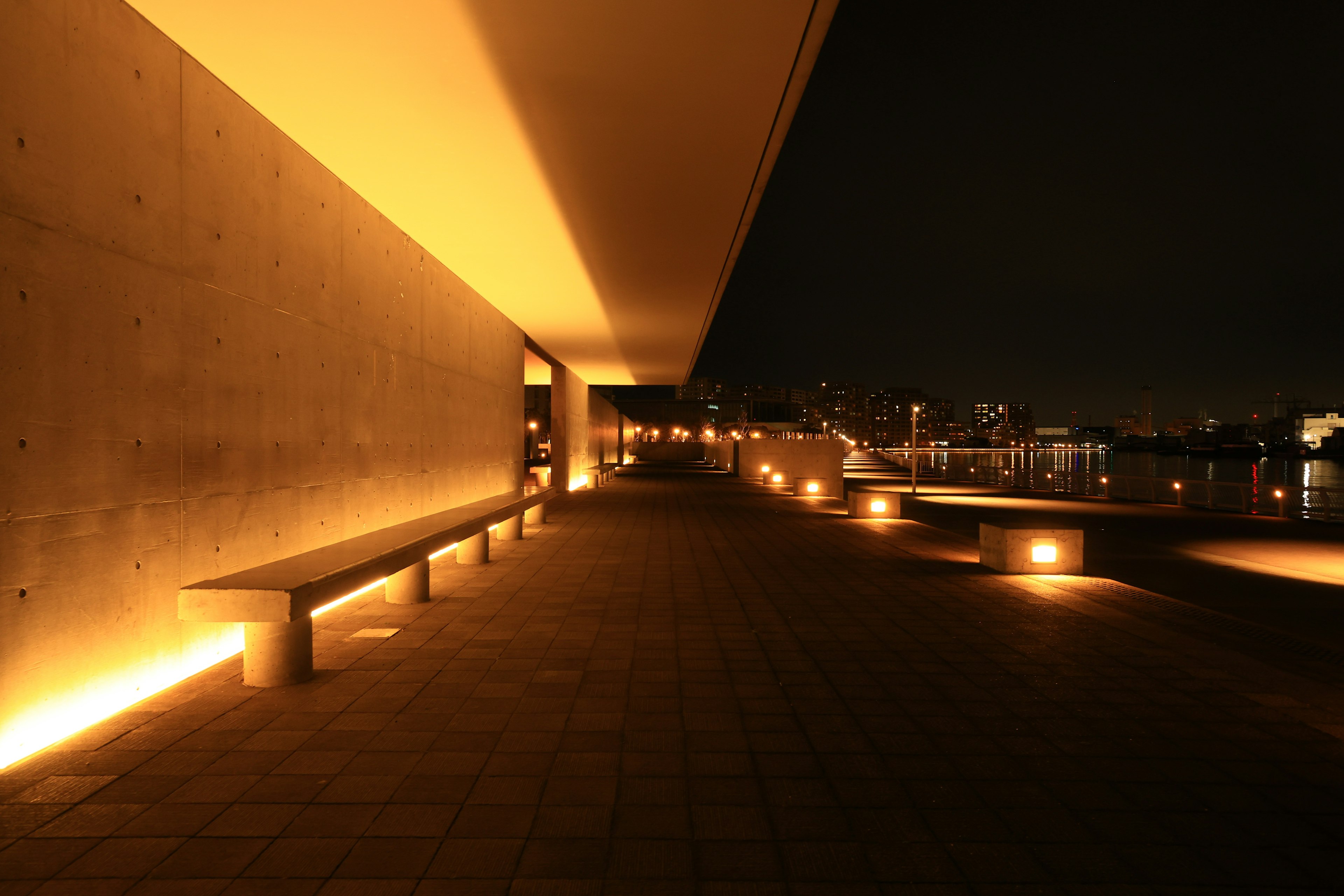 Imagen de una terraza moderna con pared de concreto e iluminación cálida con vista a una ciudad por la noche