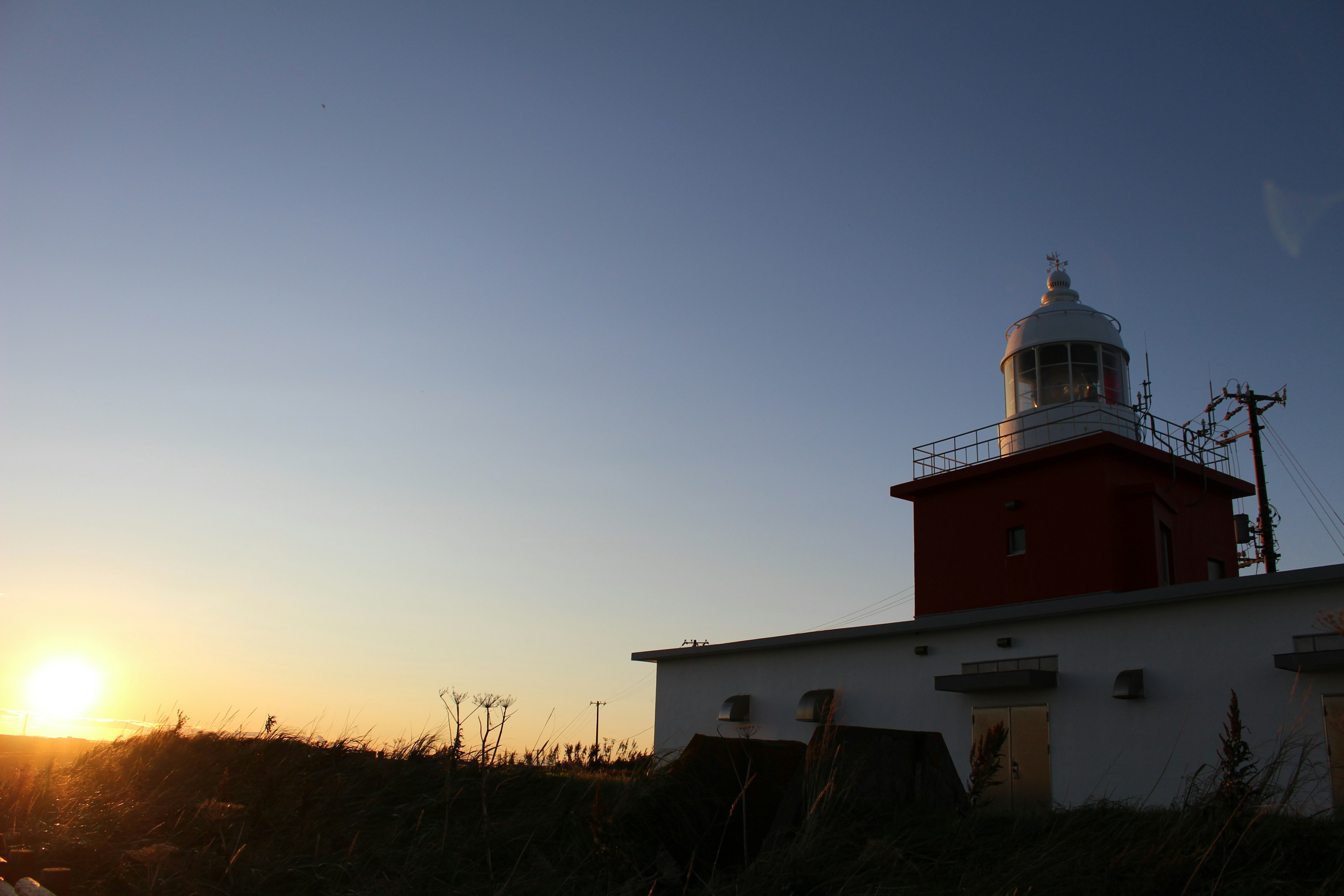 Silhouette d'un phare au coucher de soleil avec un premier plan herbeux