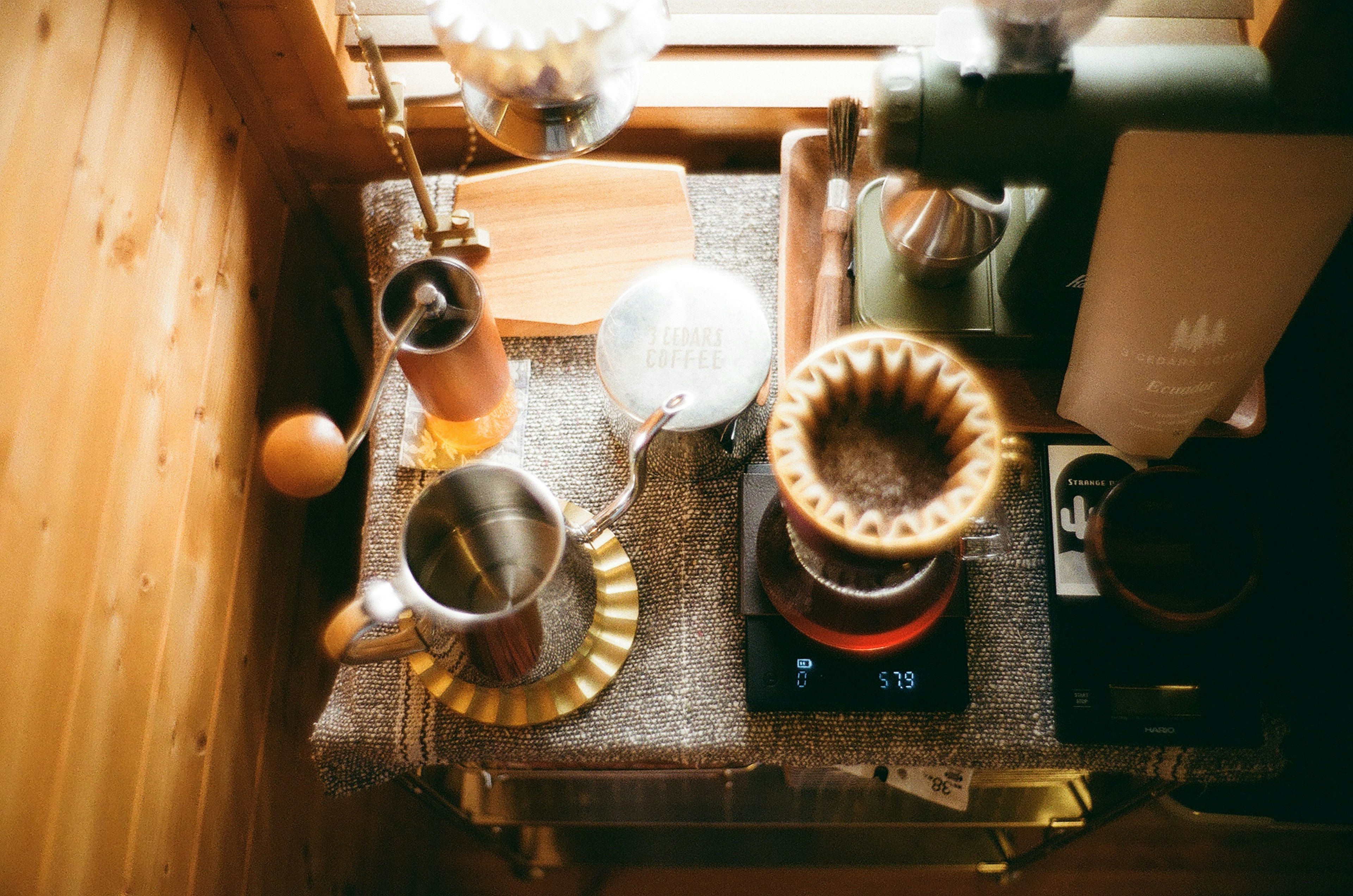 Overhead view of a wooden table with coffee brewing equipment including a dripper kettle and a bag of coffee beans