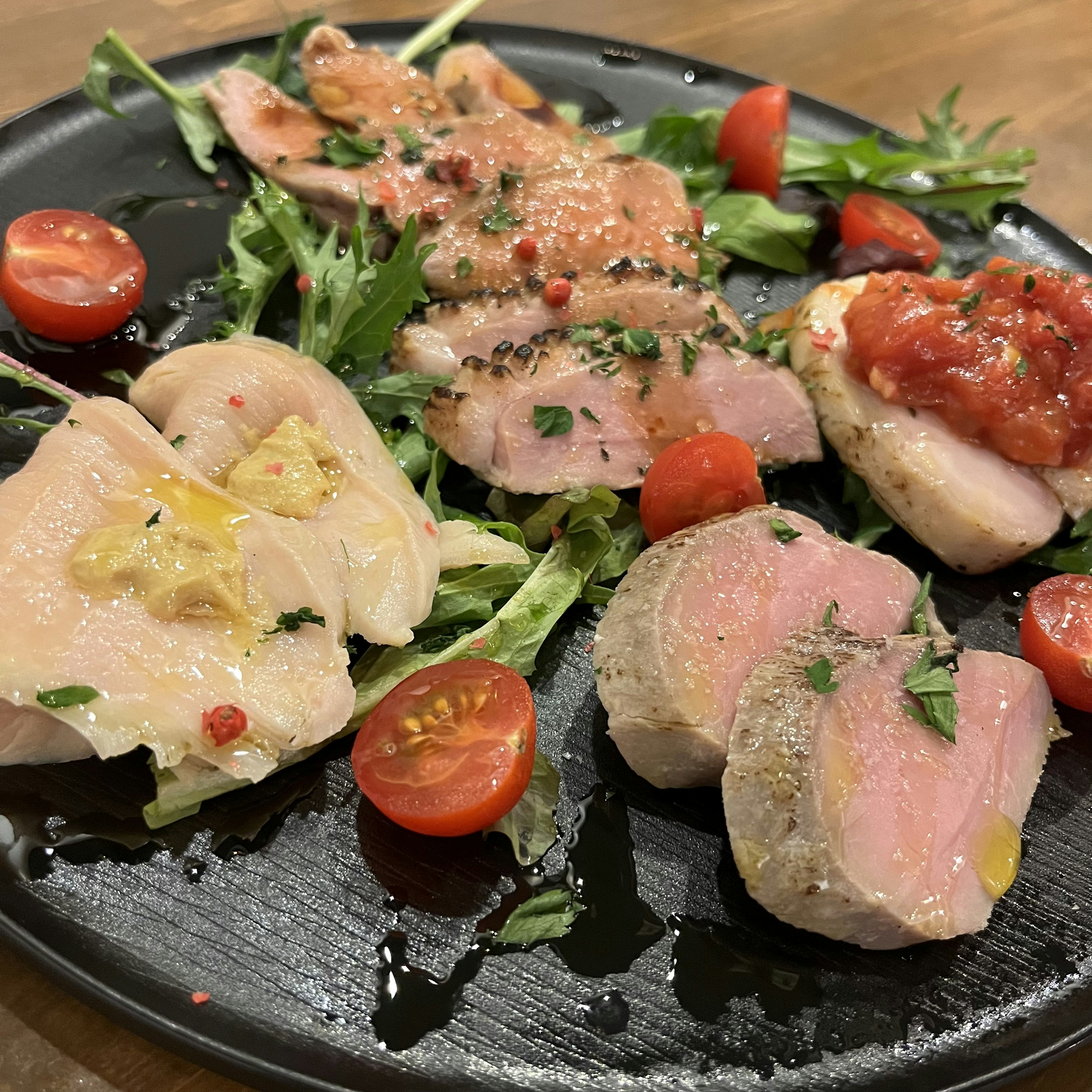 Une assiette noire avec différents plats de poulet garnis d'herbes et de tomates cerises