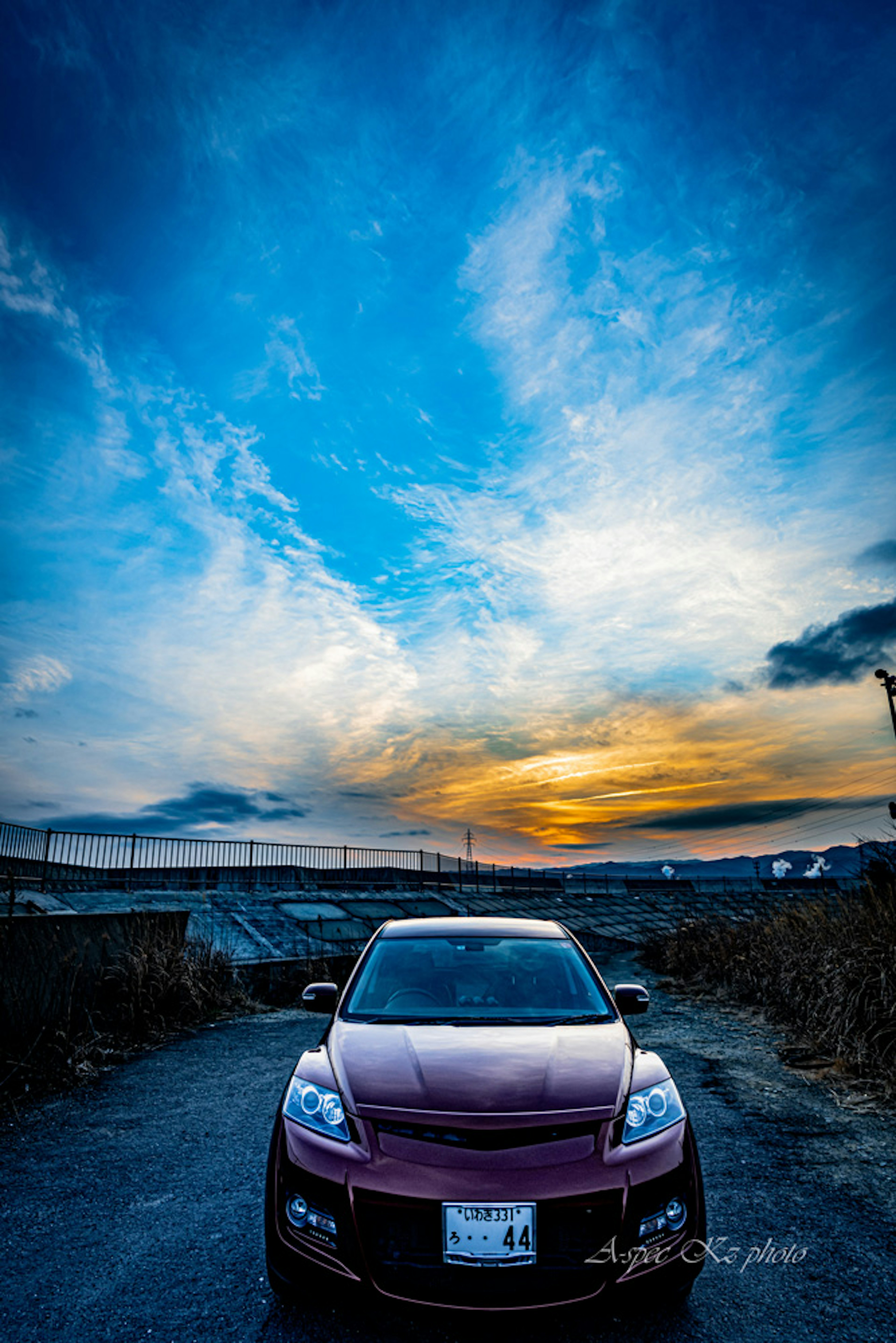 Une voiture rouge au premier plan avec un coucher de soleil vibrant et un ciel vaste