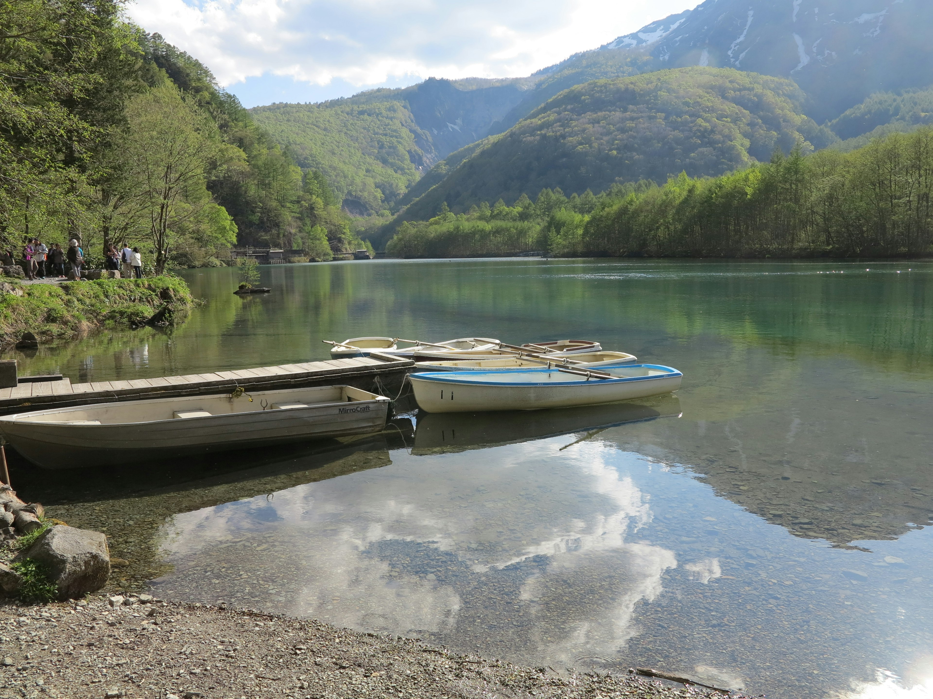 Danau tenang dengan perahu dan pantulan pegunungan sekitarnya