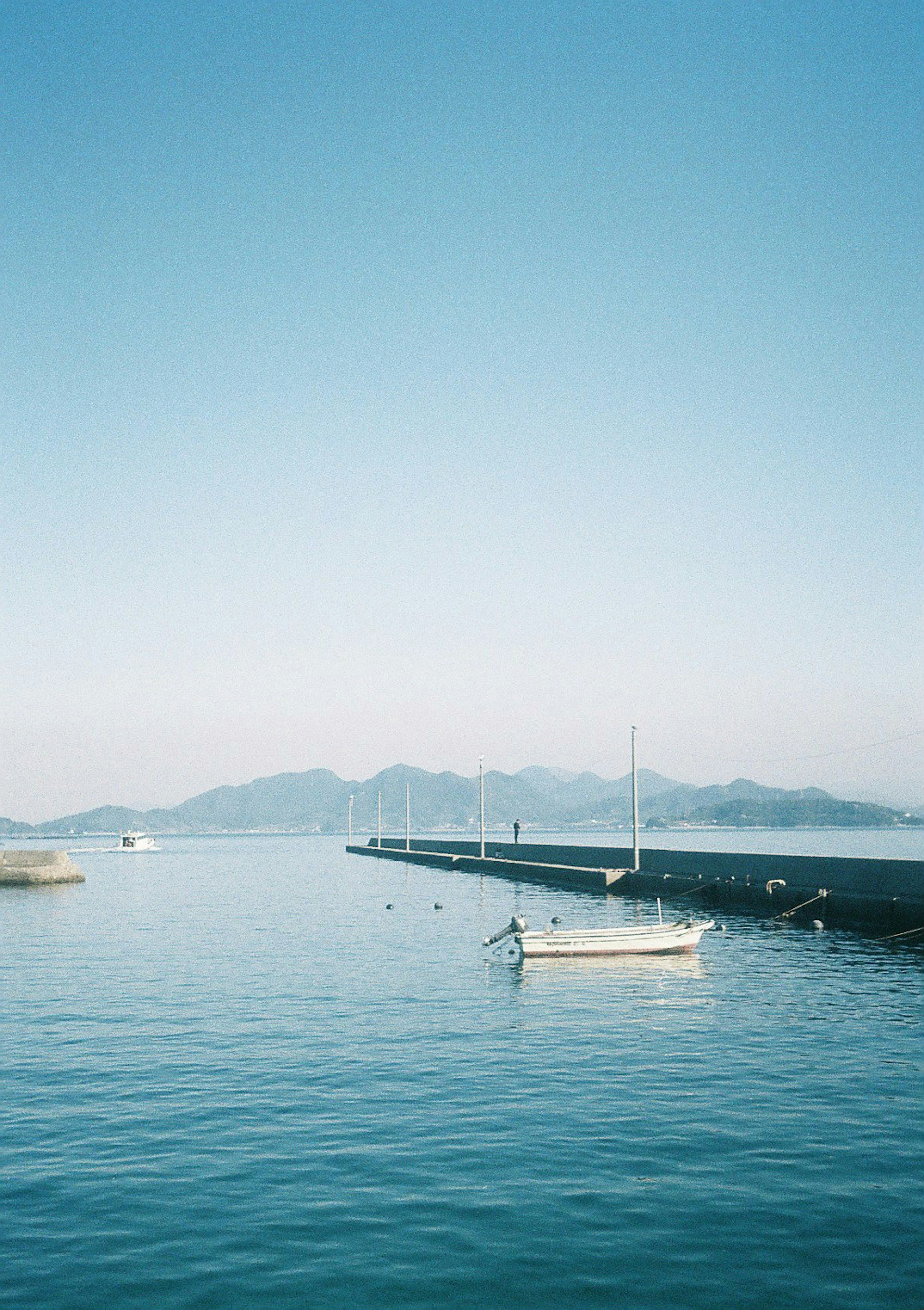 Ein kleines Boot auf ruhigem Wasser unter einem blauen Himmel mit fernen Bergen