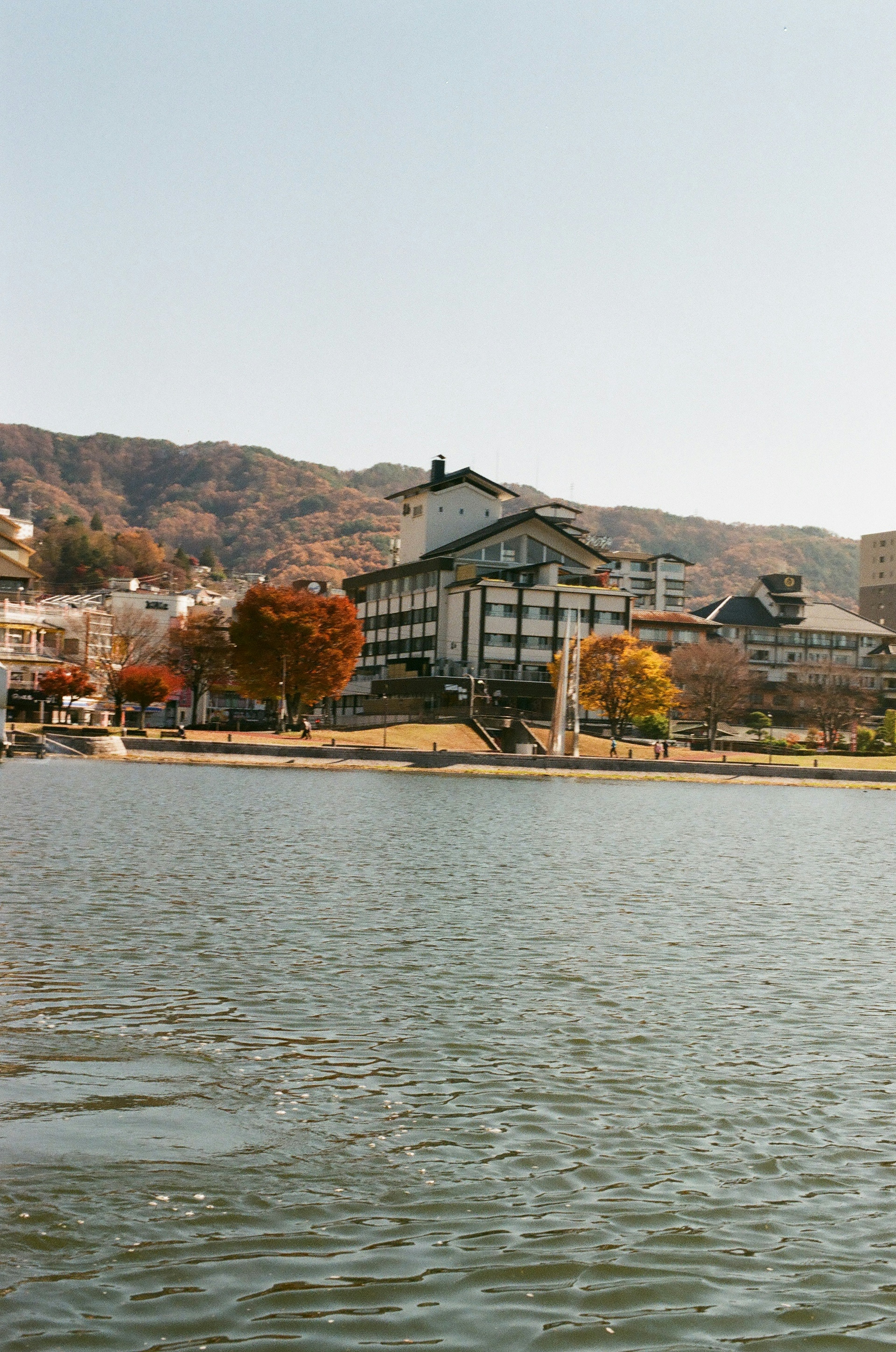 Vista escénica de una posada japonesa tradicional junto al lago con follaje de otoño y montañas