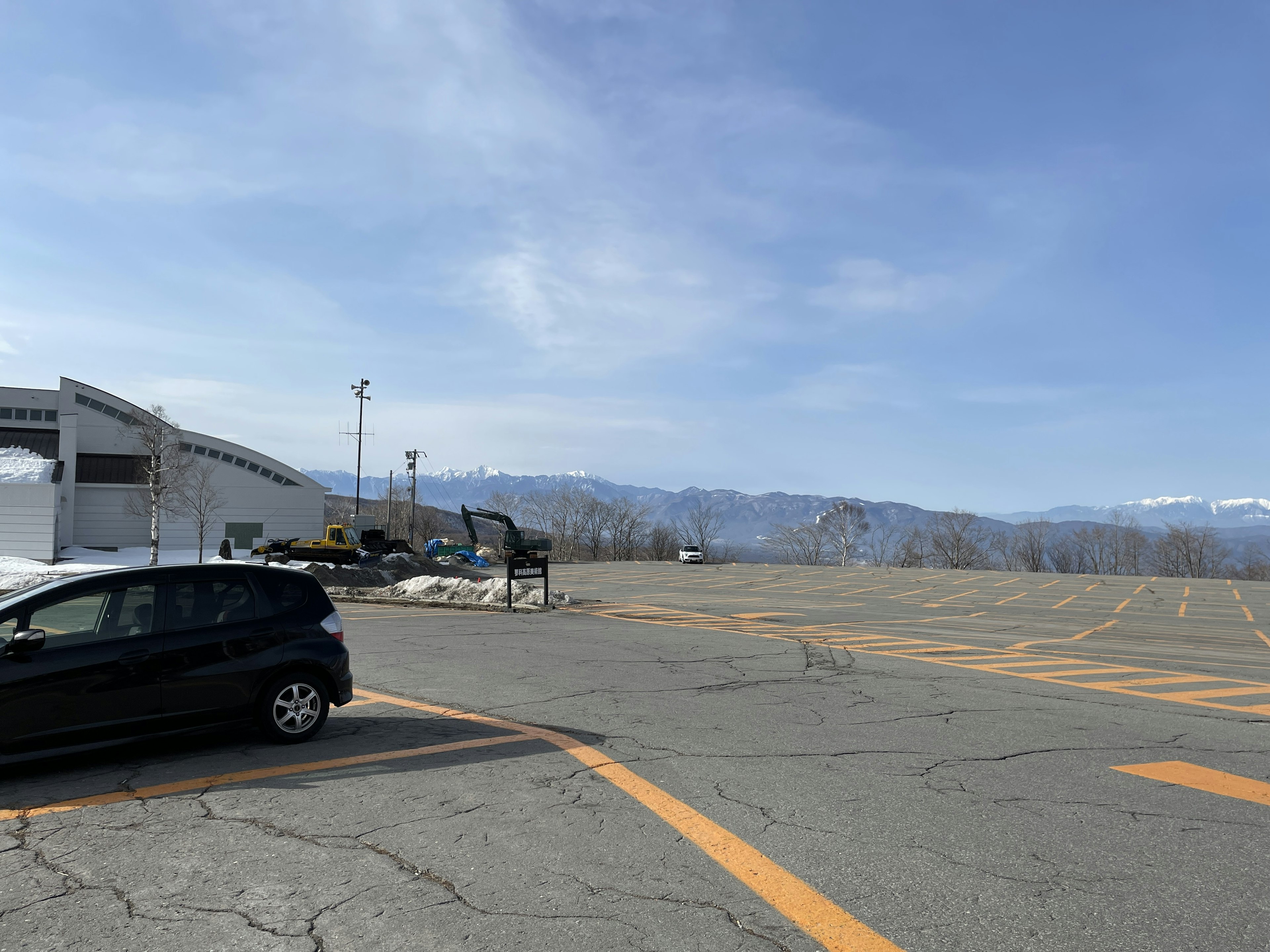 Parking lot with a clear blue sky and snow-capped mountains in the background featuring a black car