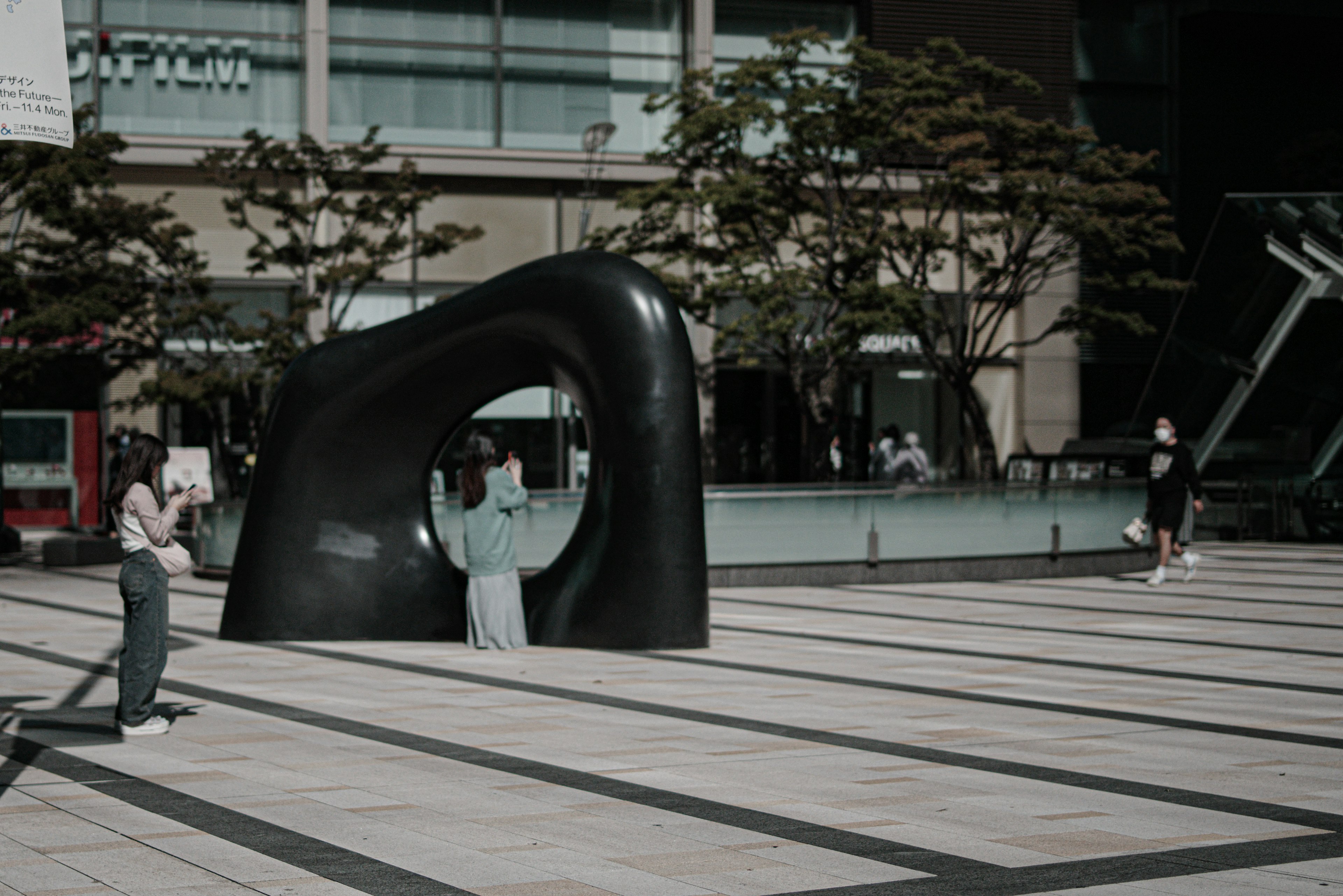 Une femme posant devant une sculpture noire avec des gens marchant autour