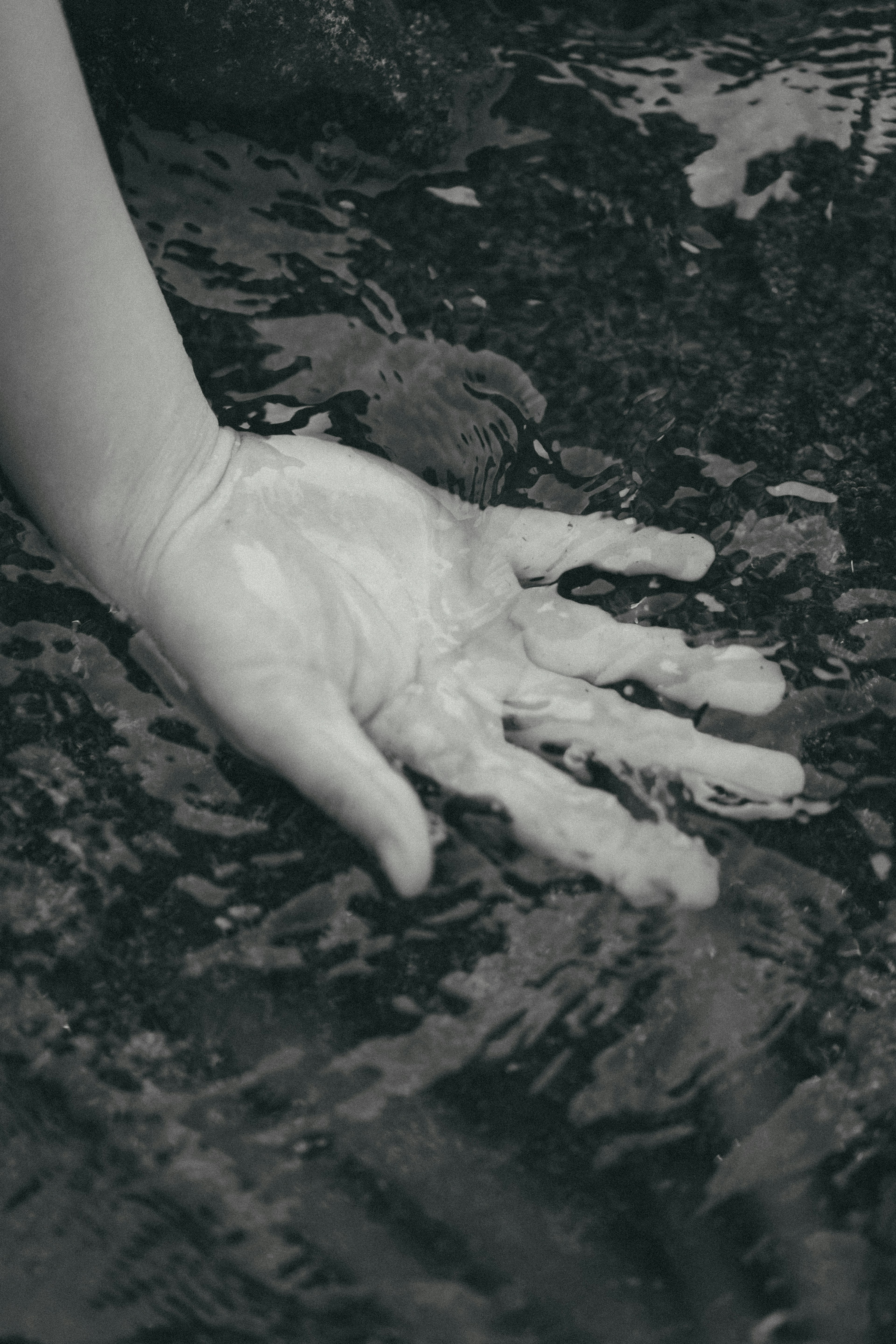 A hand reaching into water in black and white