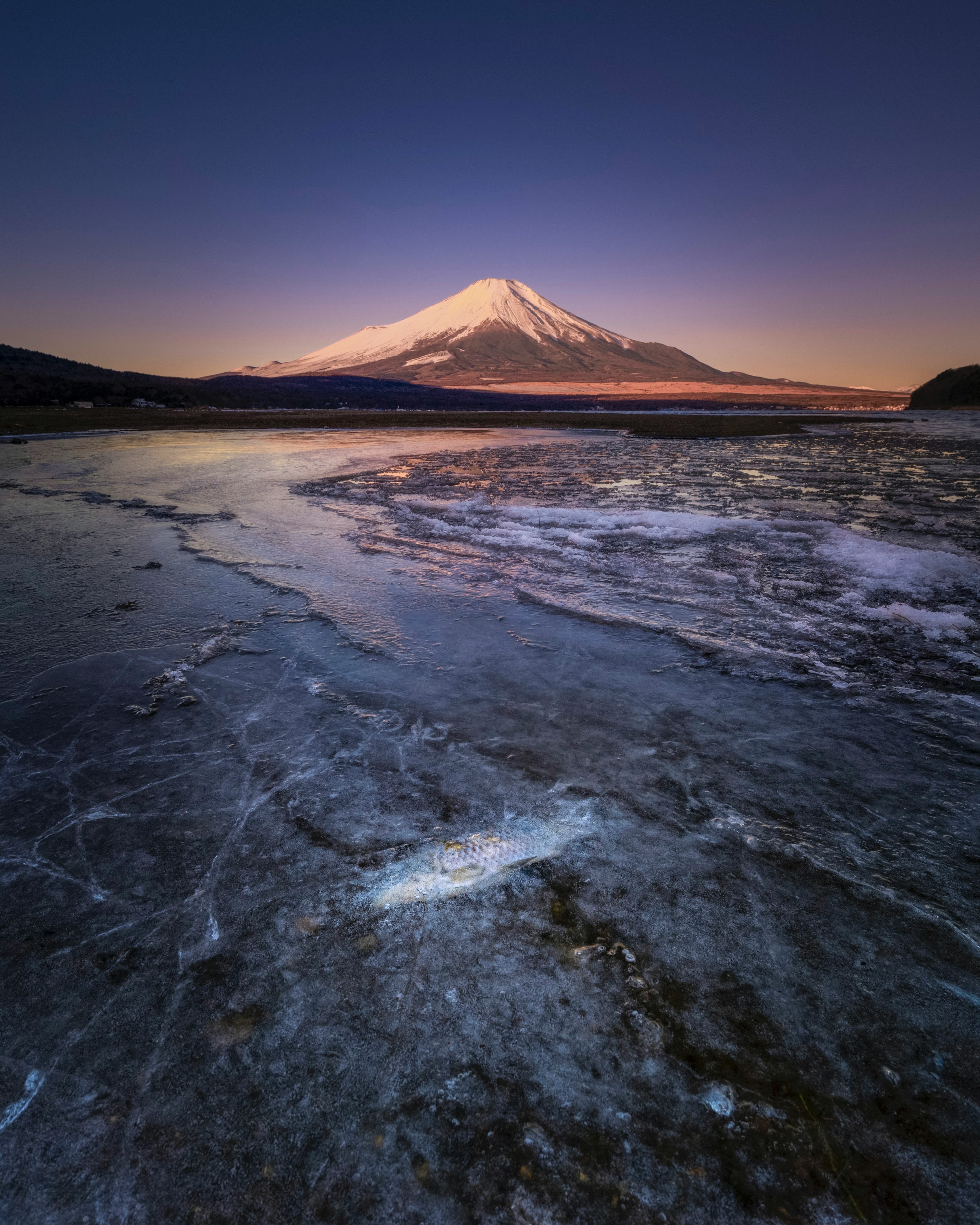 Bellissimo Monte Fuji coperto di neve vicino a un lago tranquillo illuminato dal crepuscolo