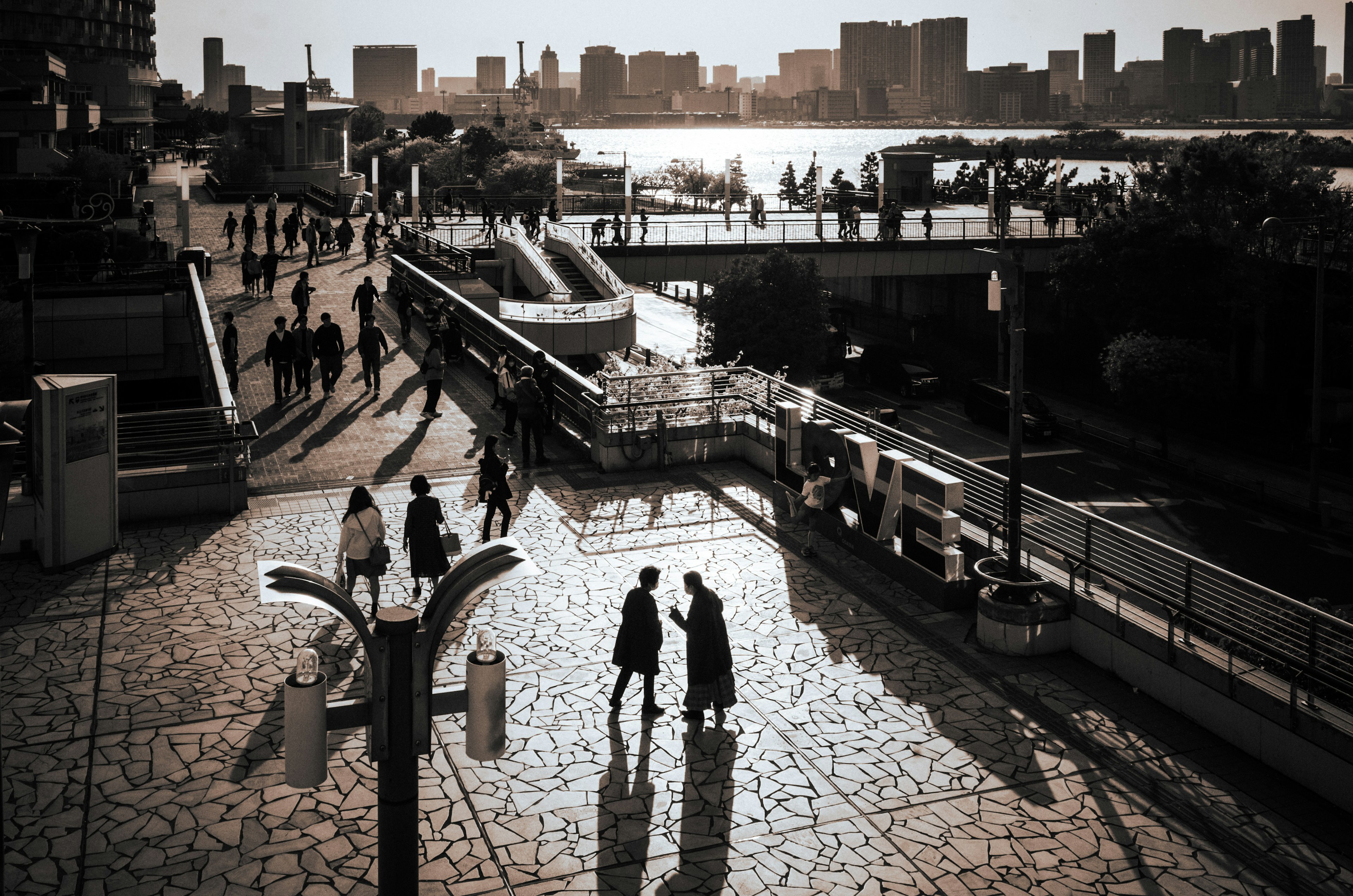 Silhouetten von Personen, die am Fluss entlang gehen, mit einer Stadtsilhouette im Hintergrund