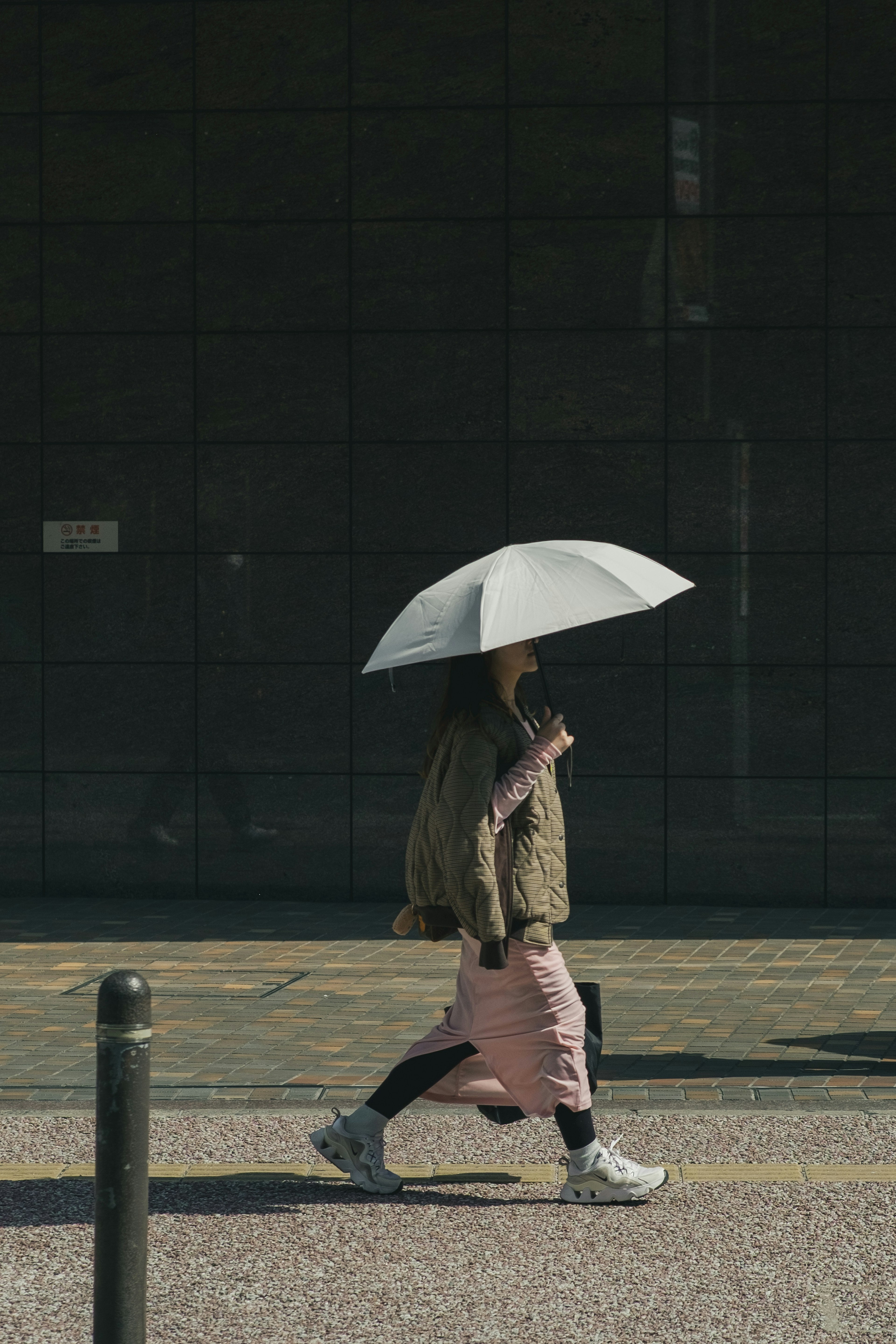 A woman walking with an umbrella against a simple modern building backdrop