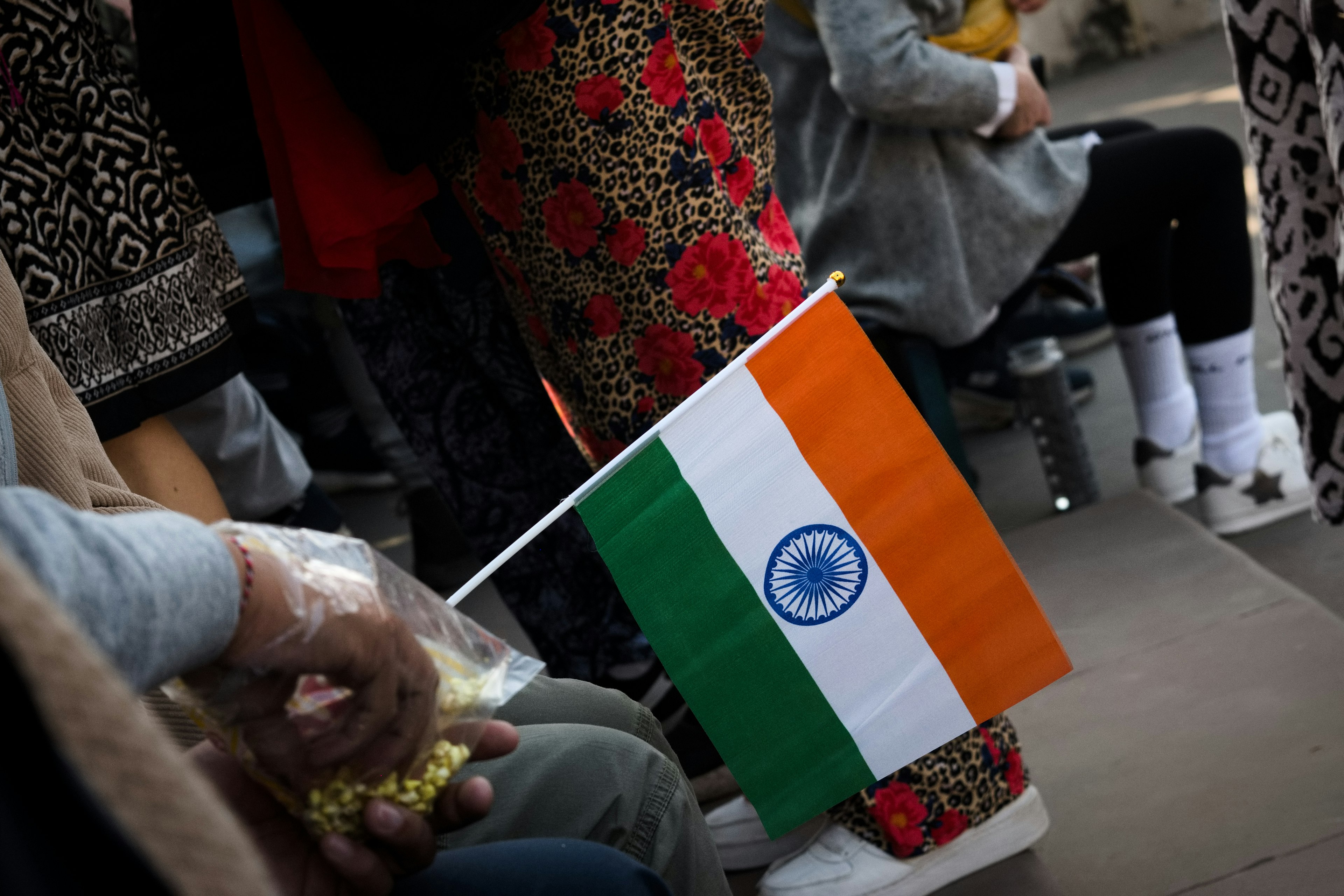 Hand holding Indian flag with colorful traditional attire in the background