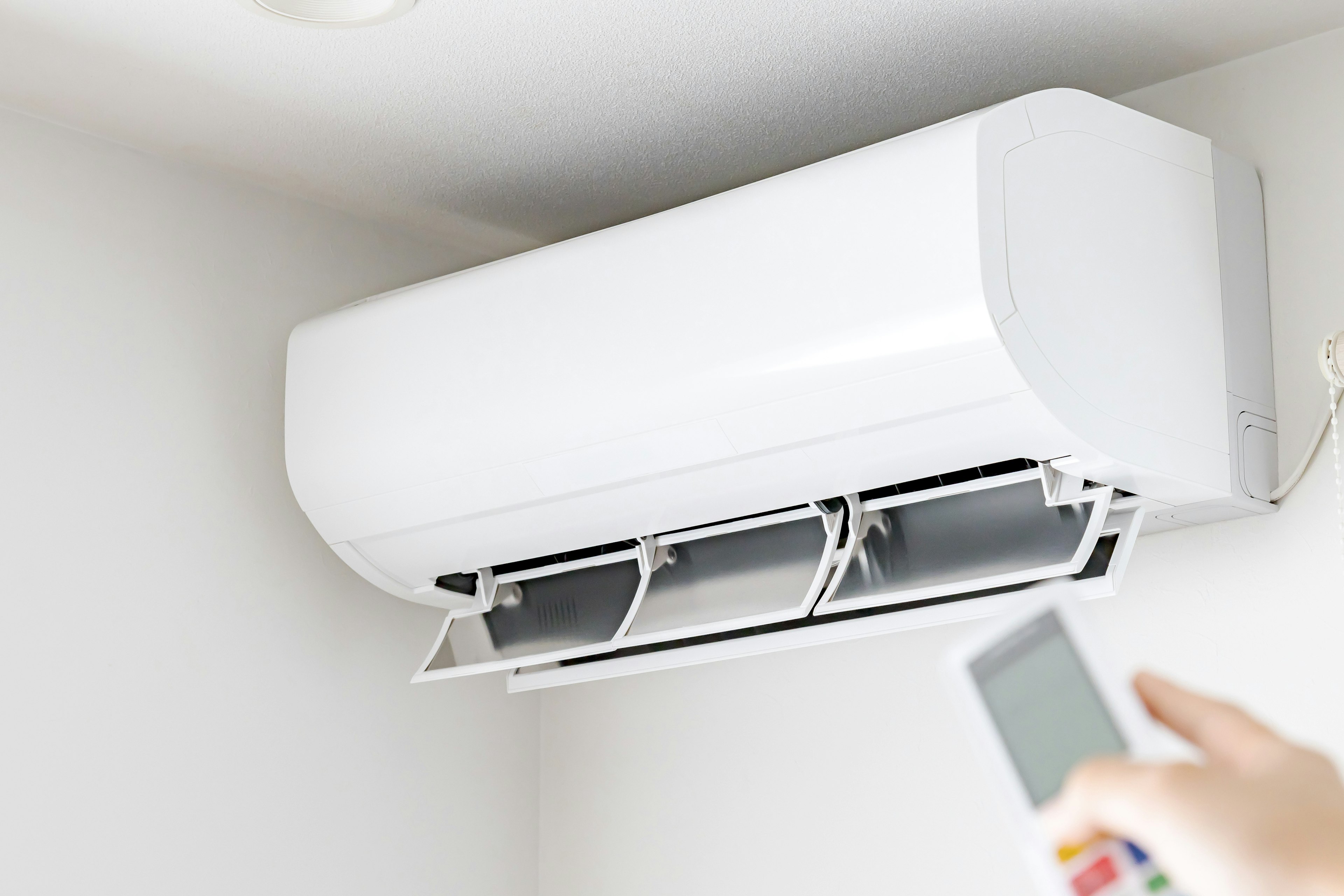 Air conditioning unit mounted on a wall with a hand holding a remote control