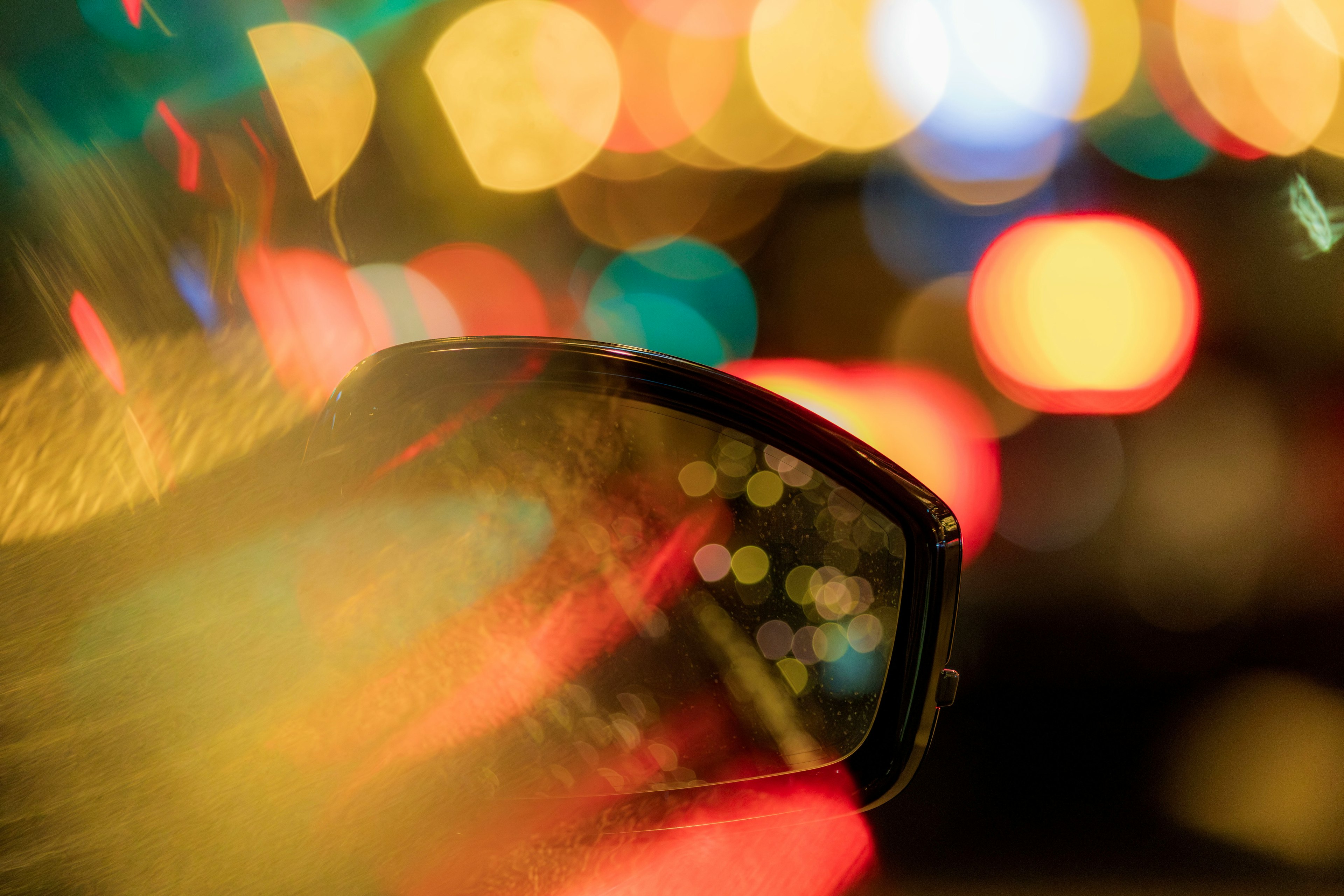 Car side mirror reflecting blurred city lights at night