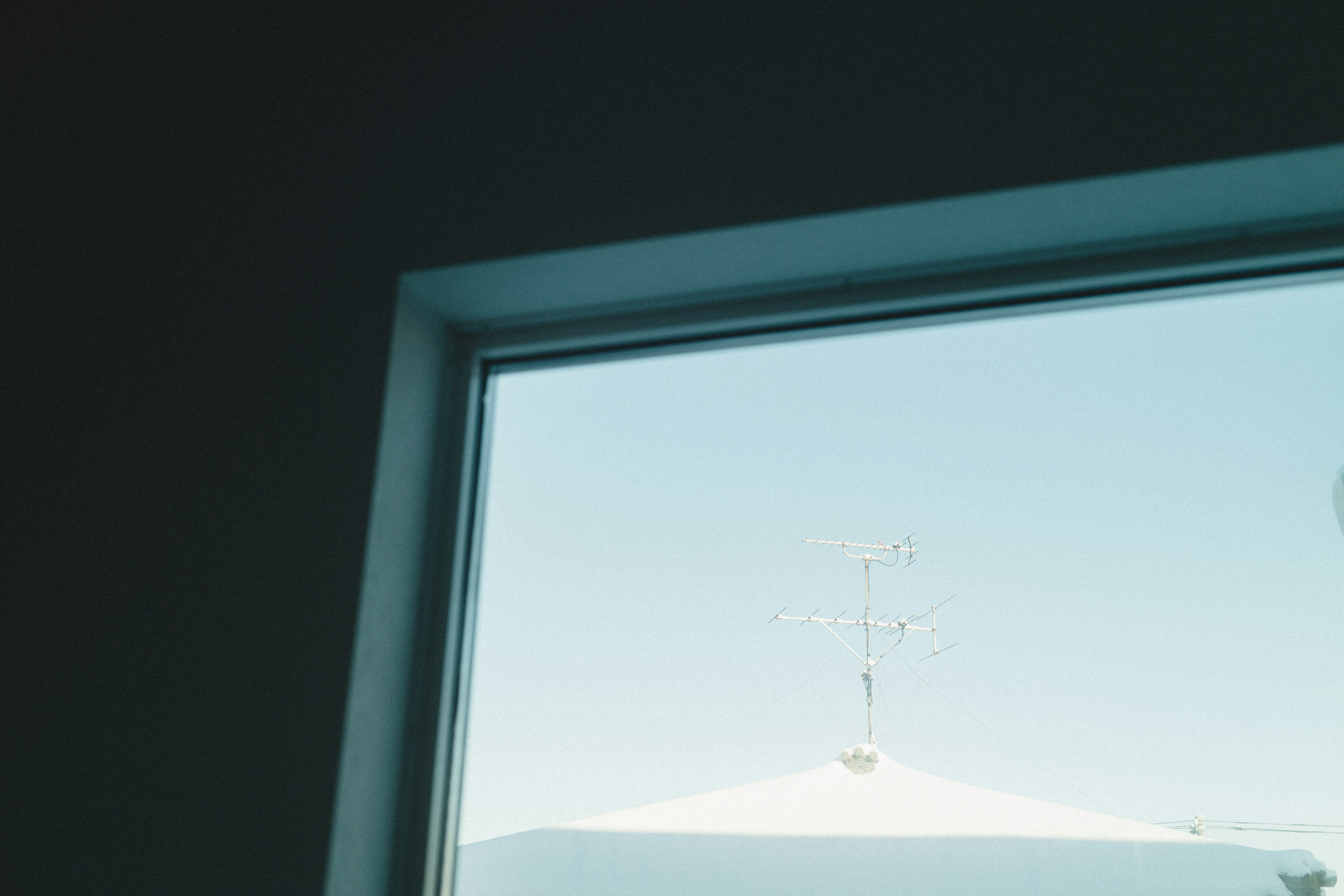 Blick auf den blauen Himmel und einen Teil eines Daches durch ein Fenster