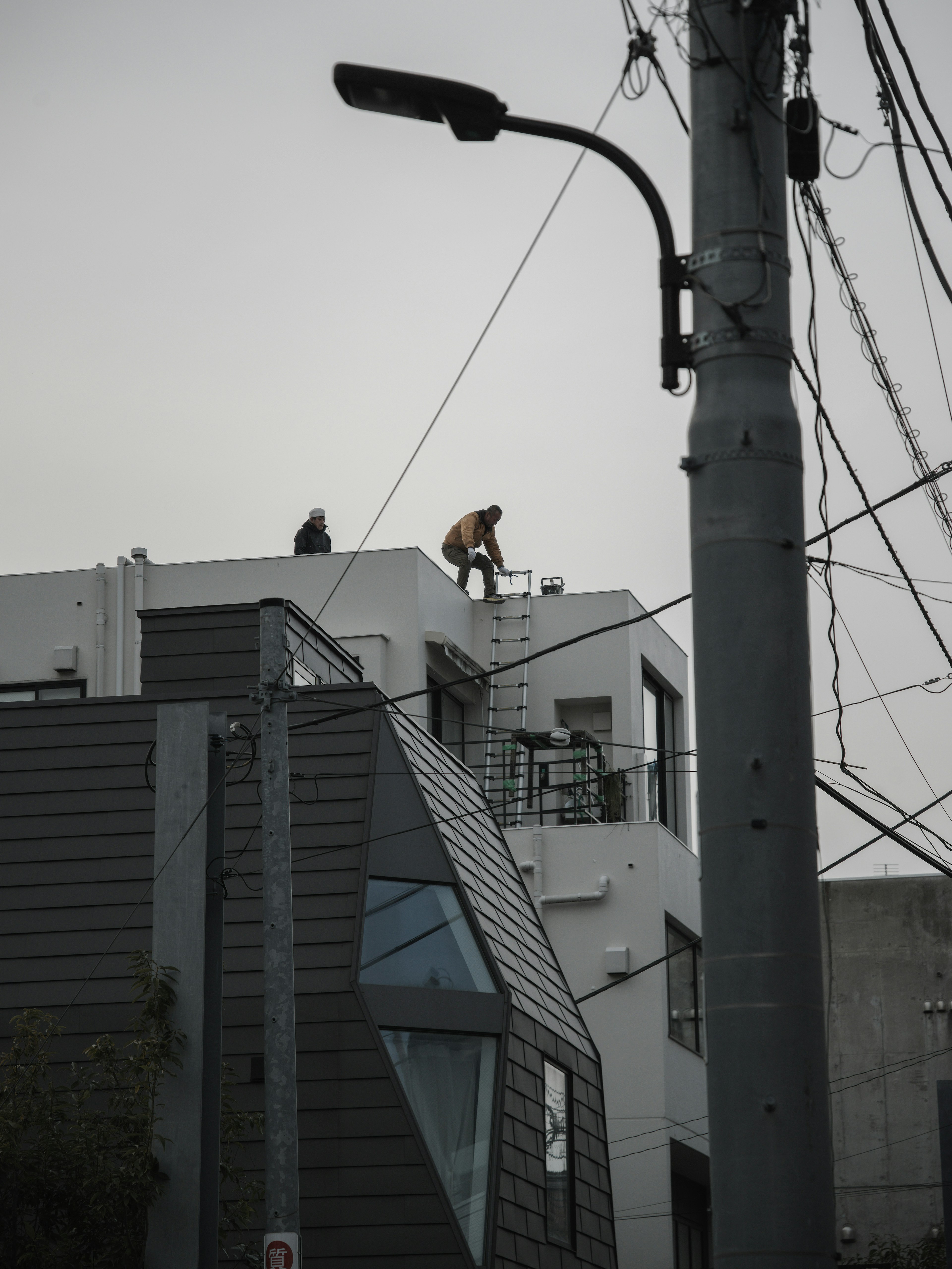 屋根の上で作業する人と近くの建物の特徴を示す灰色の空の画像