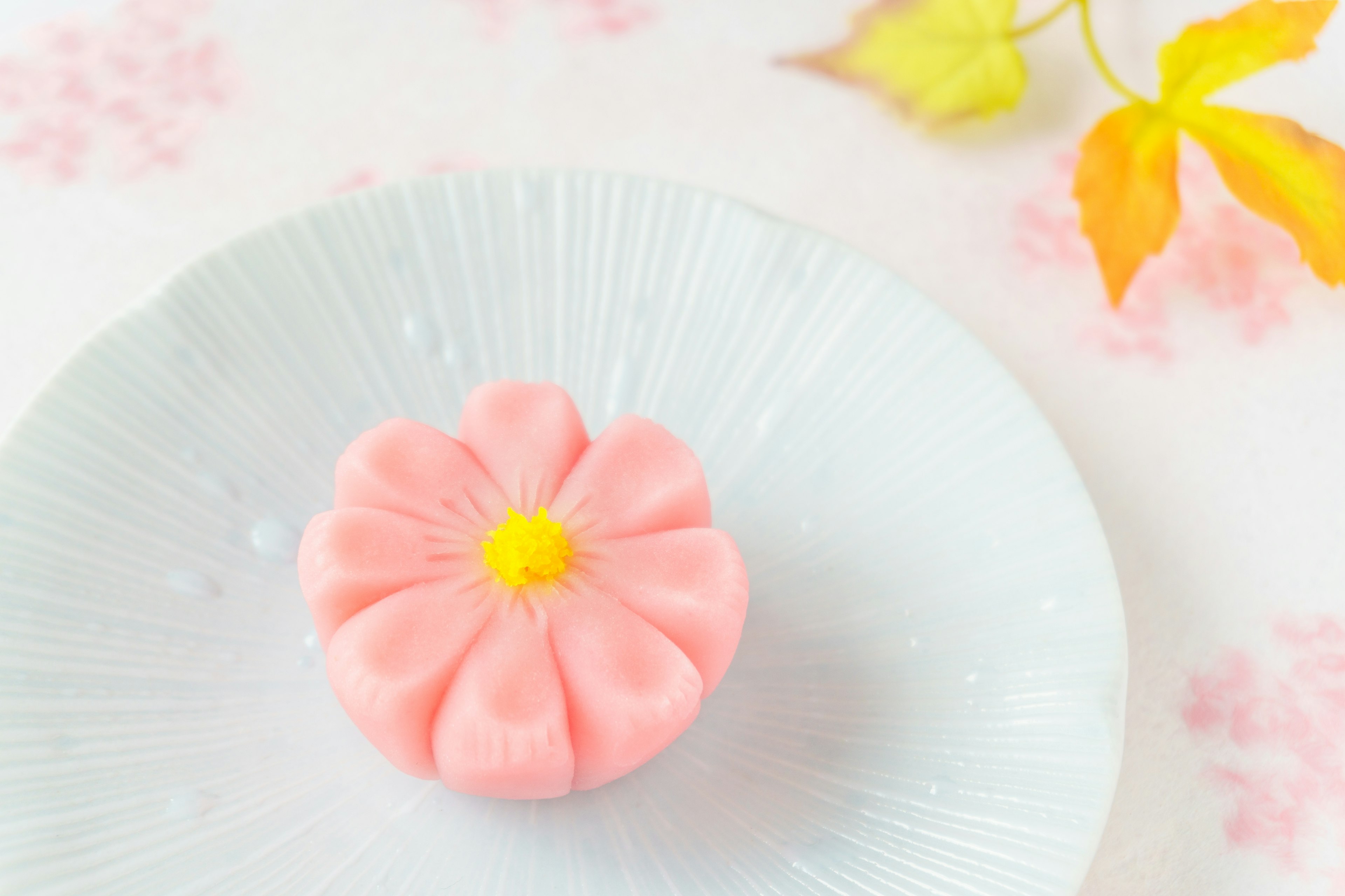 Kue wagashi berbentuk bunga merah muda di piring biru muda