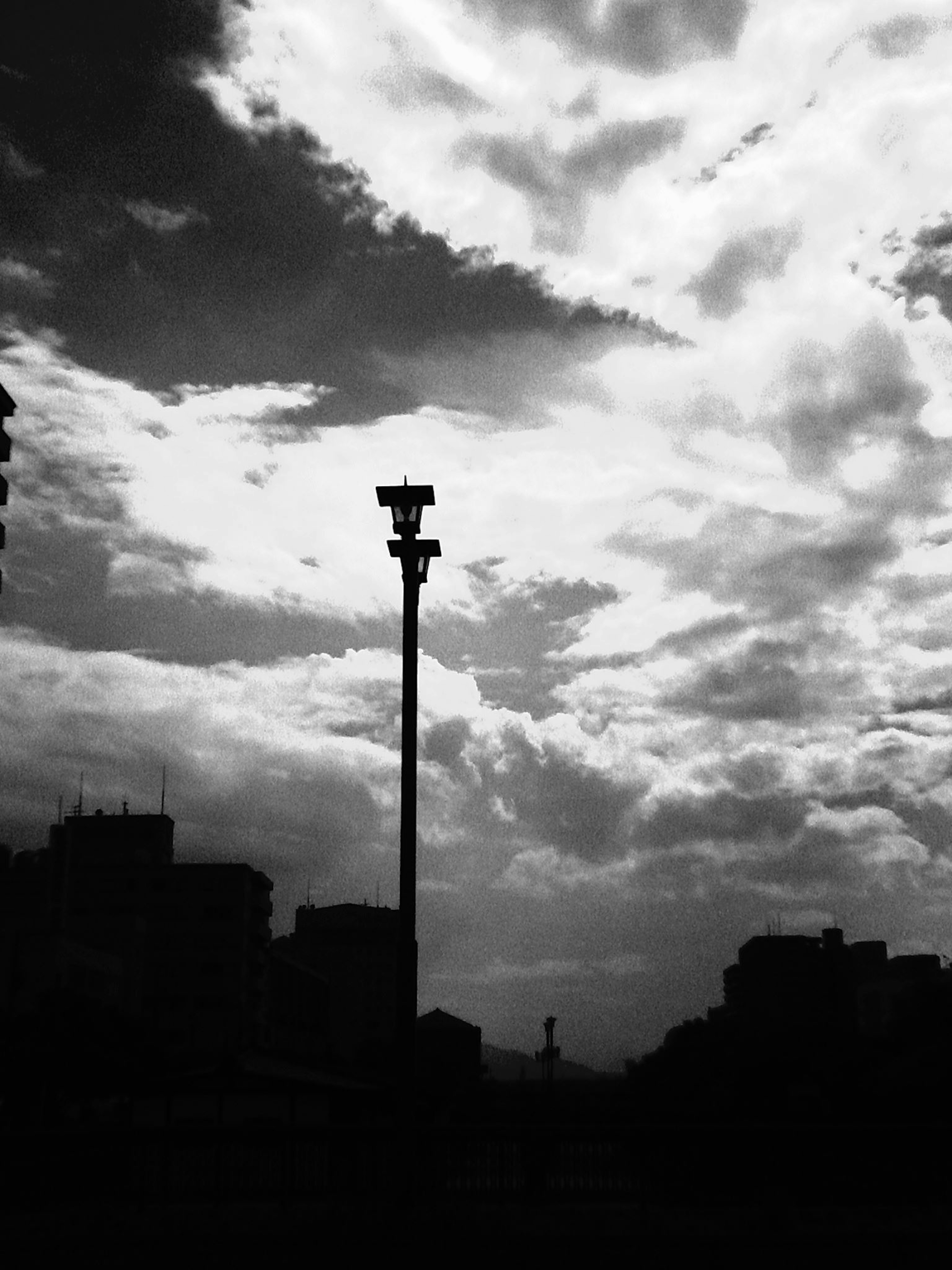 Silhouette of a streetlight against a dramatic black and white sky