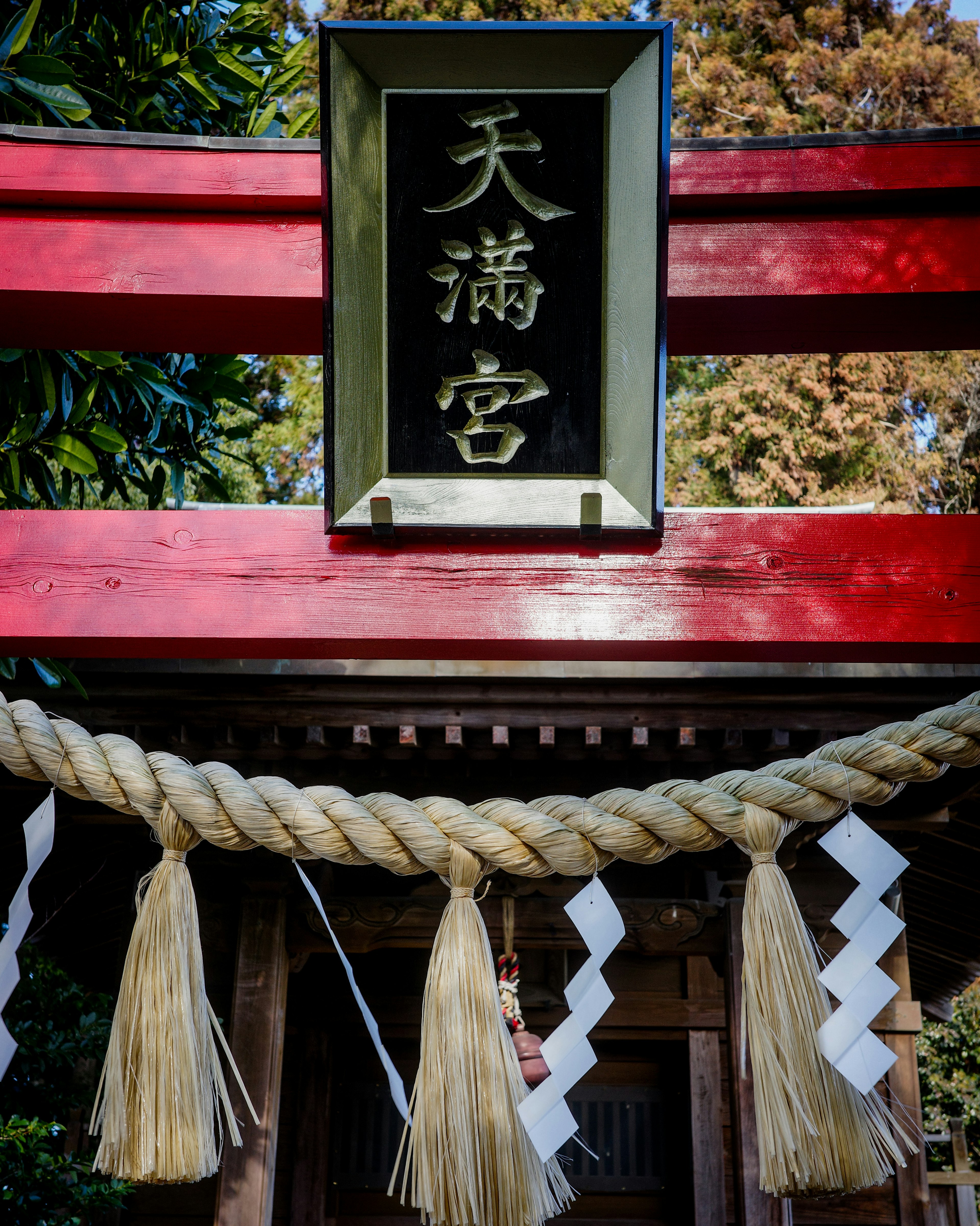 Ein lebendiges rotes Torii mit einem Schild, das den Tenmangu-Schrein anzeigt, geschmückt mit traditionellen Shide