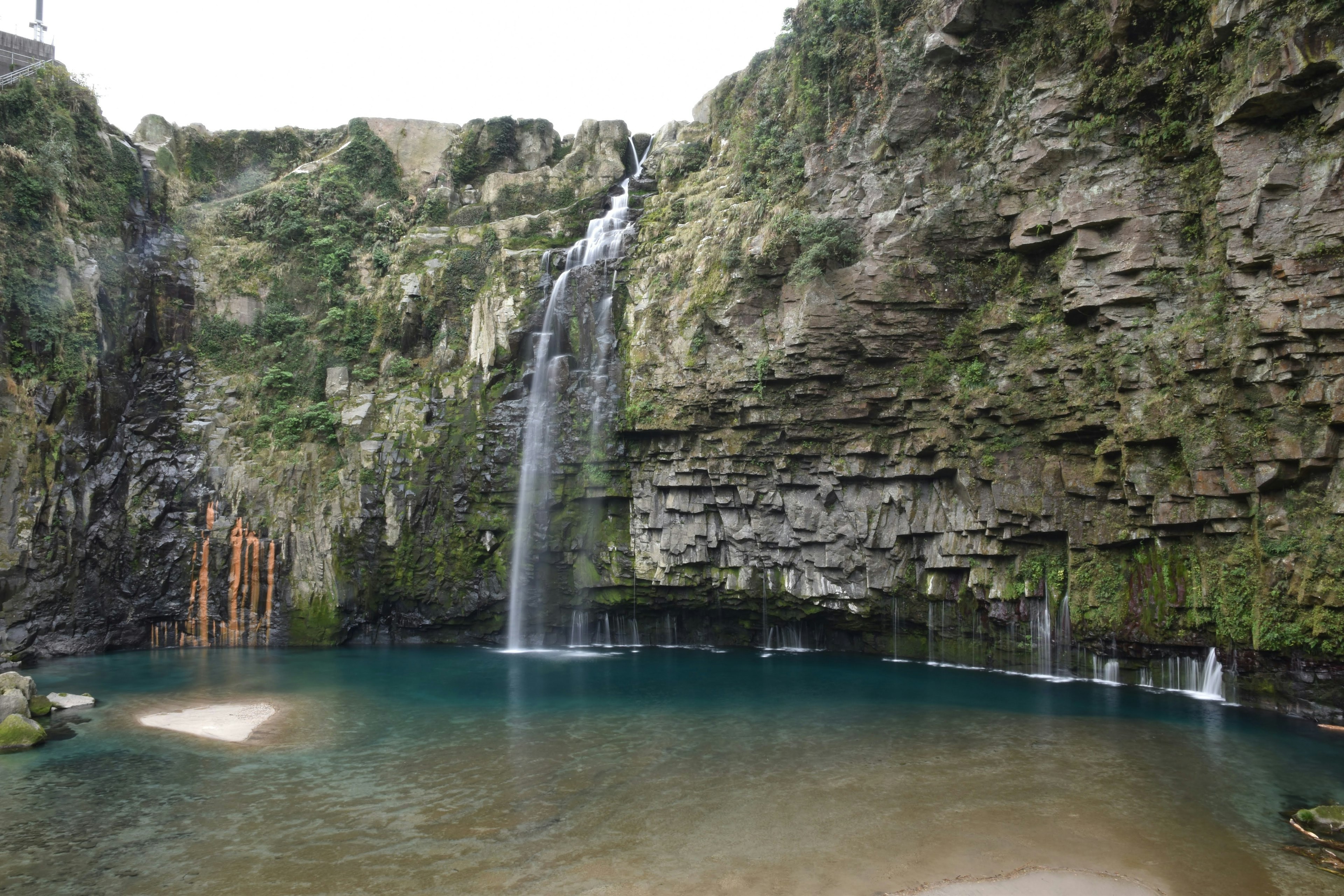 Une belle cascade tombant sur des falaises verdoyantes dans une piscine bleue claire