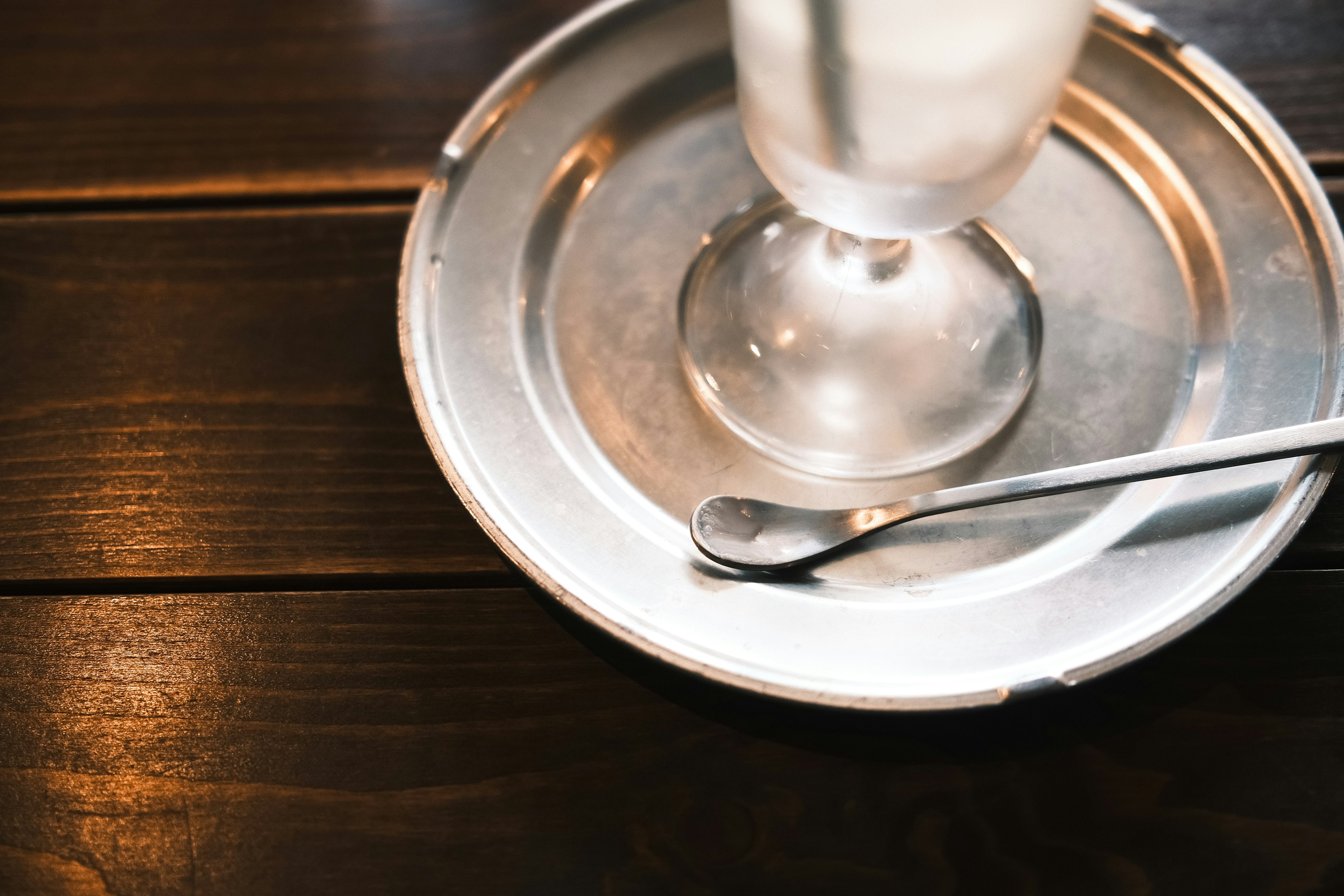 Un vaso de bebida sobre un plato de plata con una cuchara en una mesa de madera