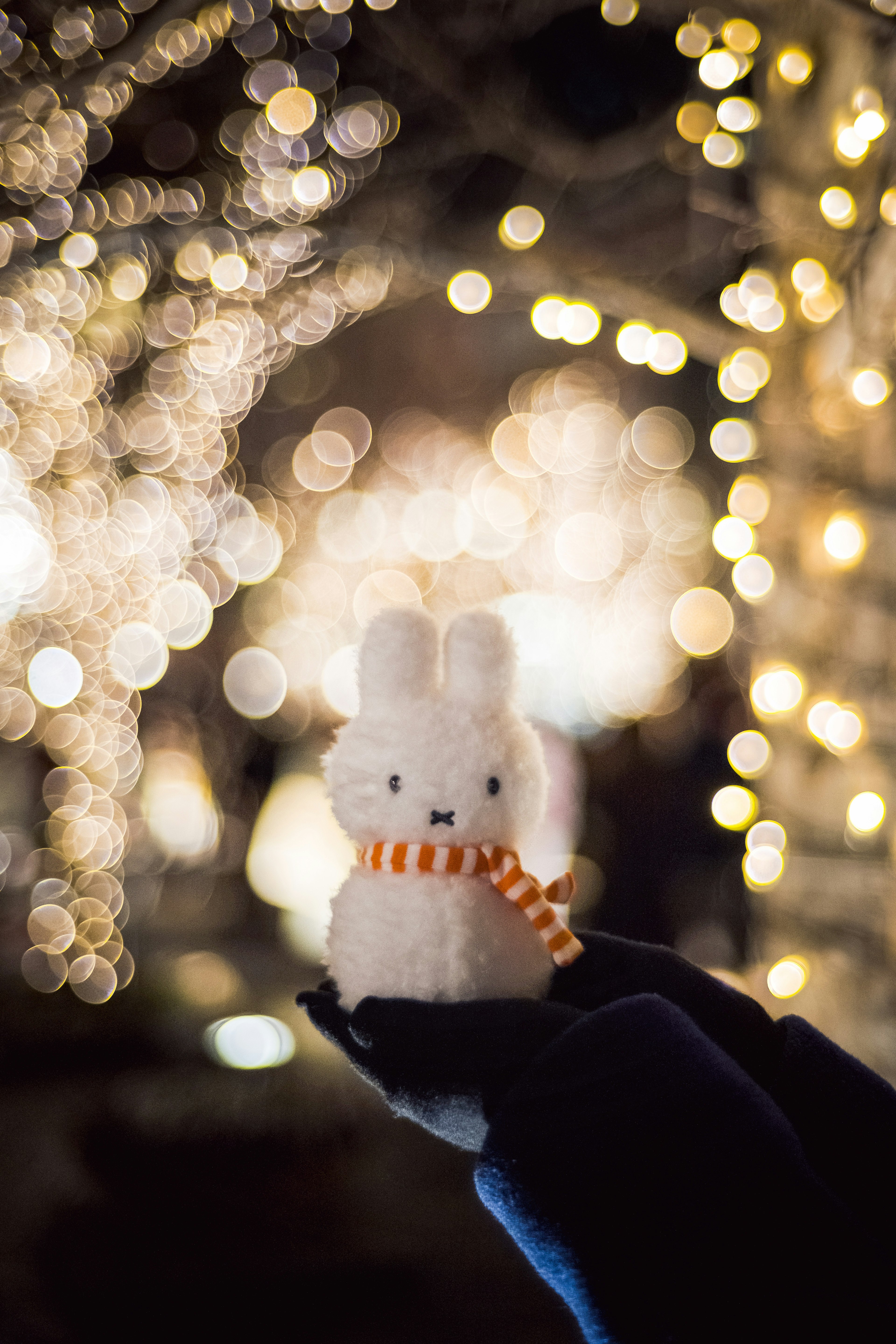 Un muñeco de peluche blanco en forma de conejo sostenido frente a luces brillantes