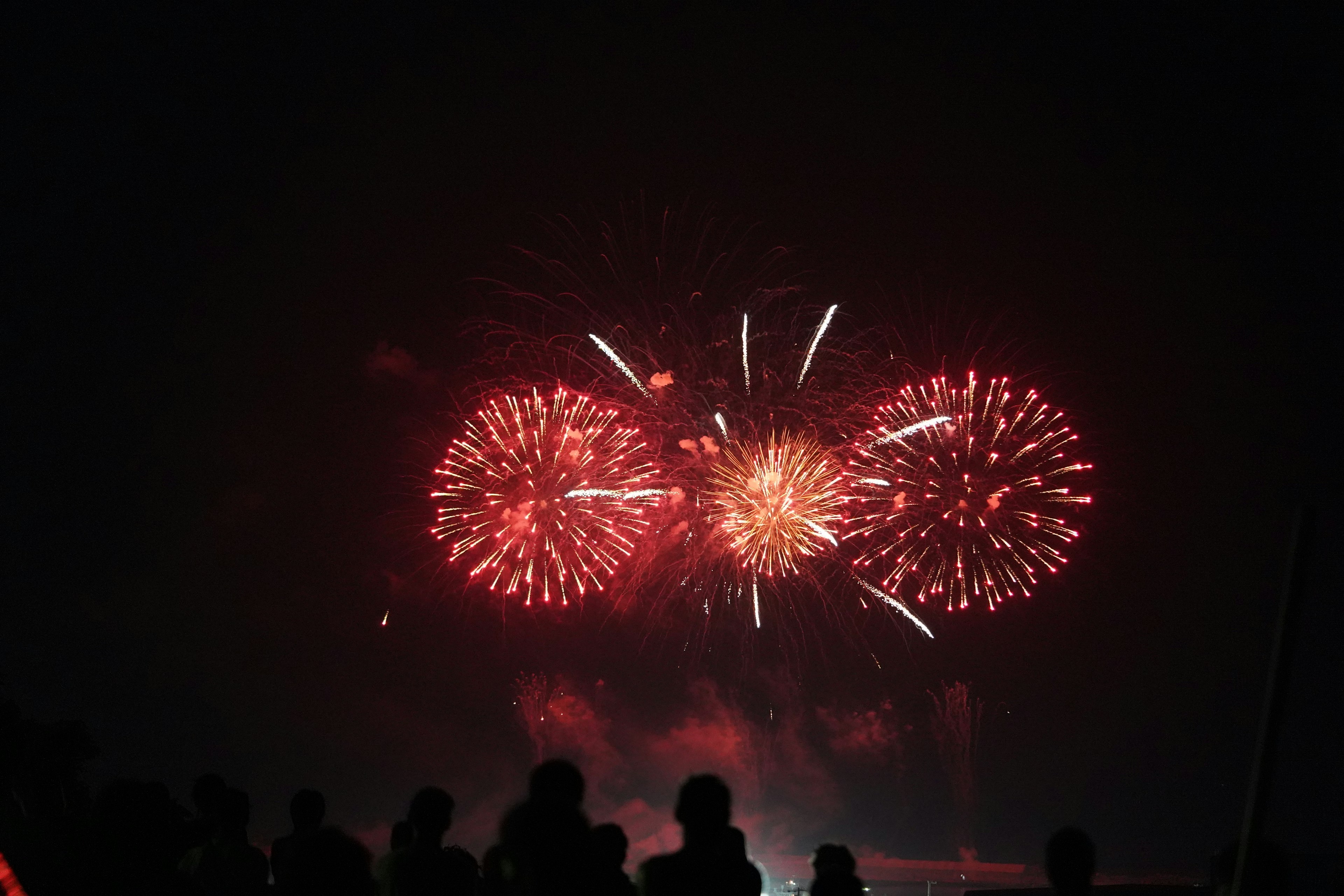 夜空に広がる赤い花火のショーとシルエットの観客