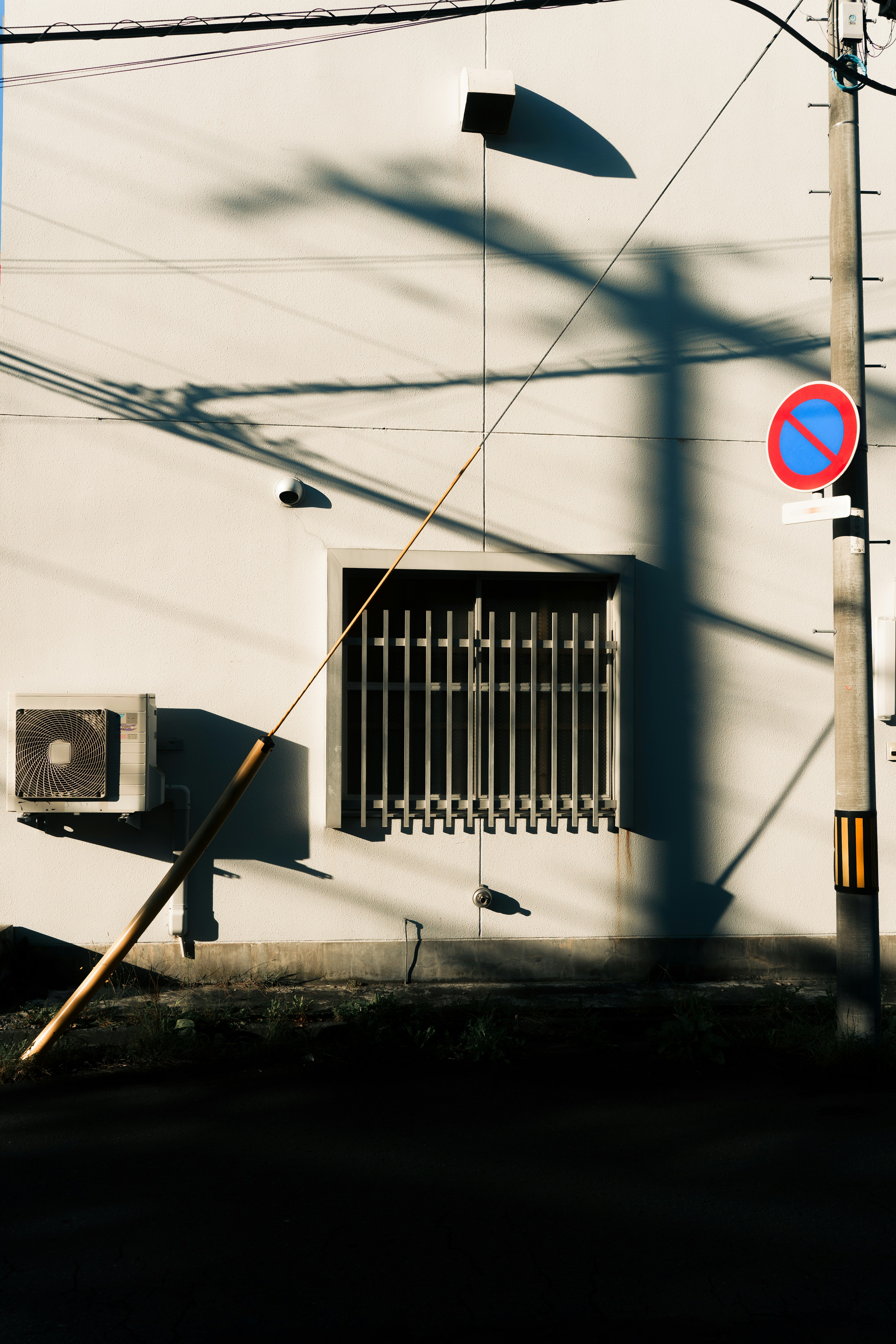 Imagen de una ventana con sombras en una pared blanca y un poste de luz