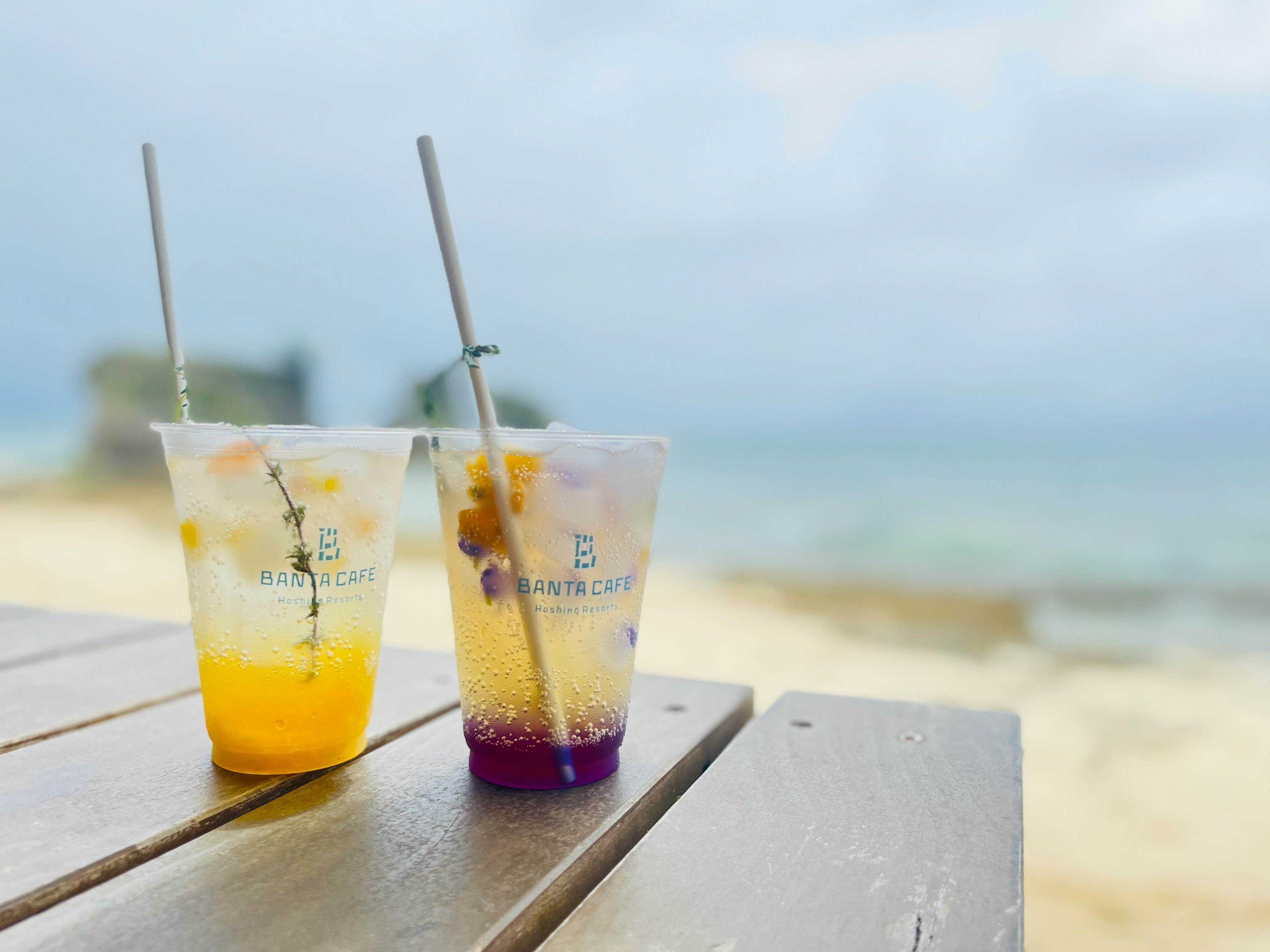 Dua gelas minuman berwarna diletakkan di dekat pantai