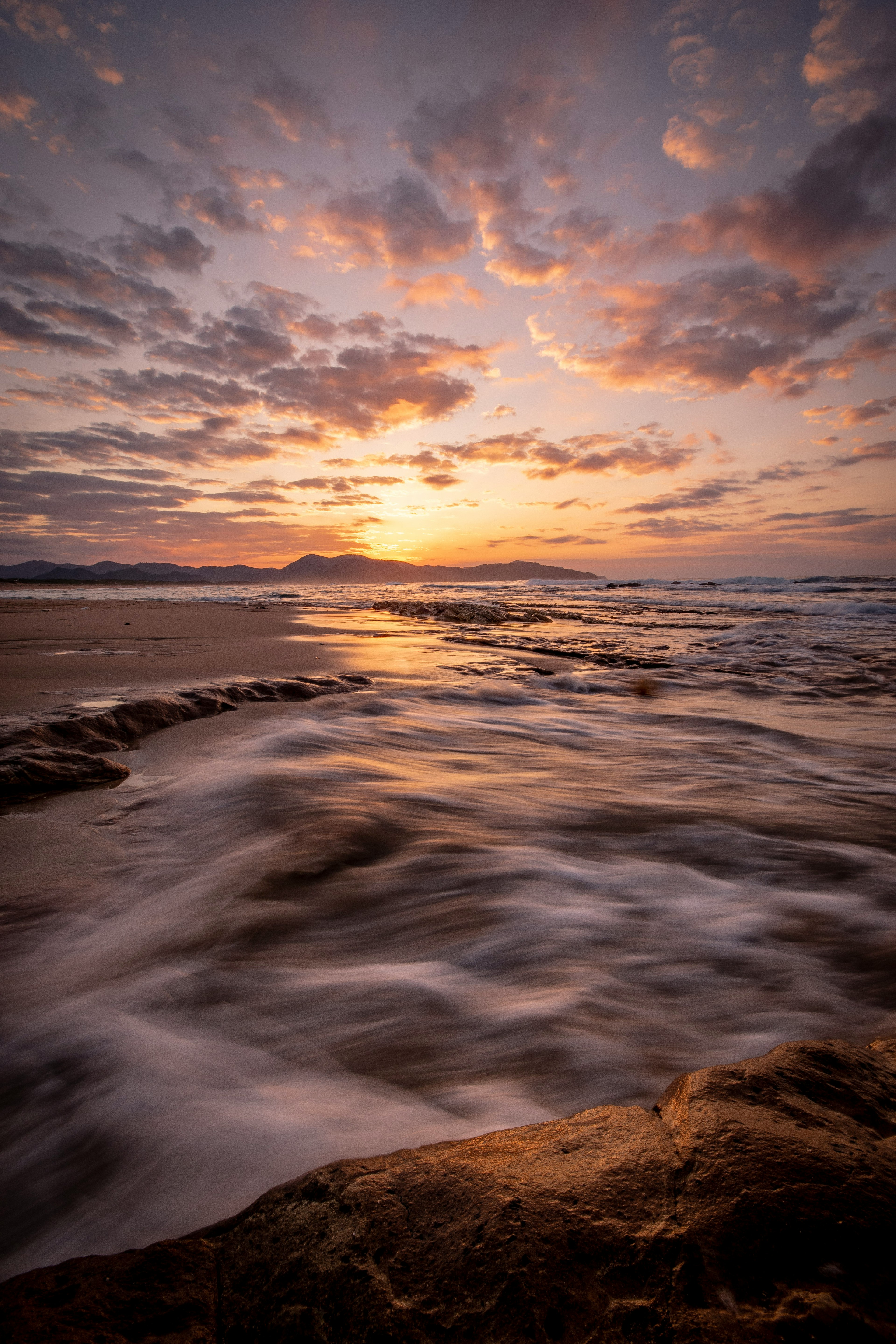 Olas fluyentes al atardecer a lo largo de la costa con texturas rocosas