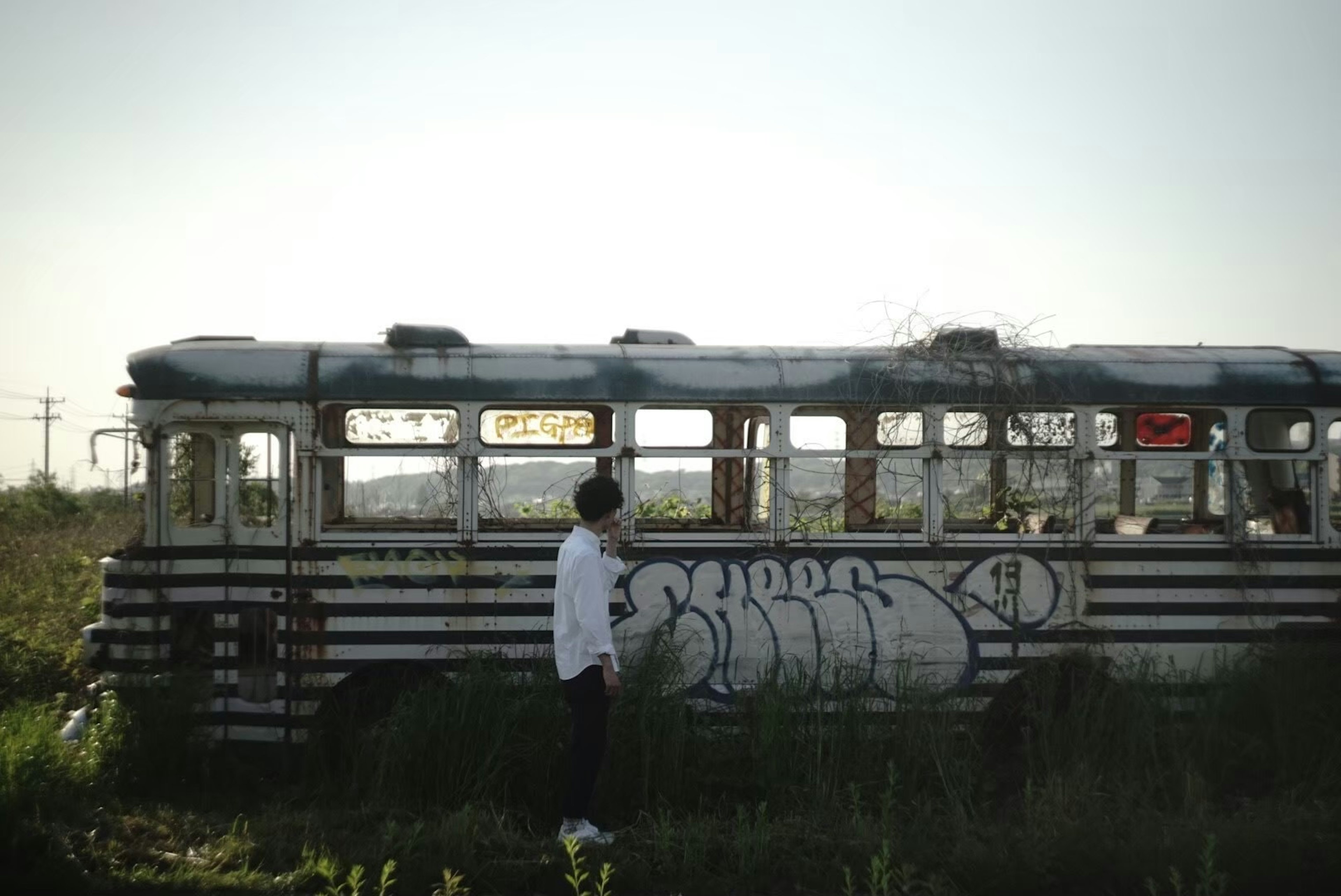 Vecchio autobus coperto di graffiti in un campo con una persona in camicia bianca