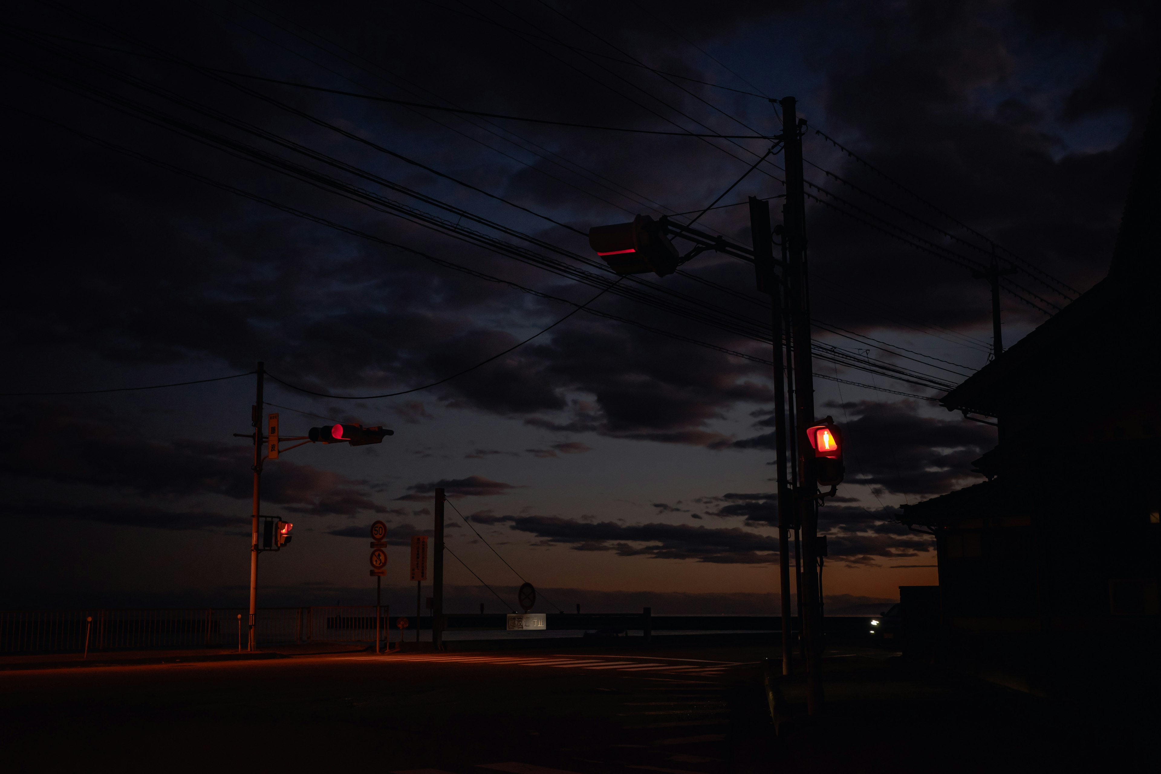 Twilight scene at a street corner with utility poles and traffic lights against a darkening sky