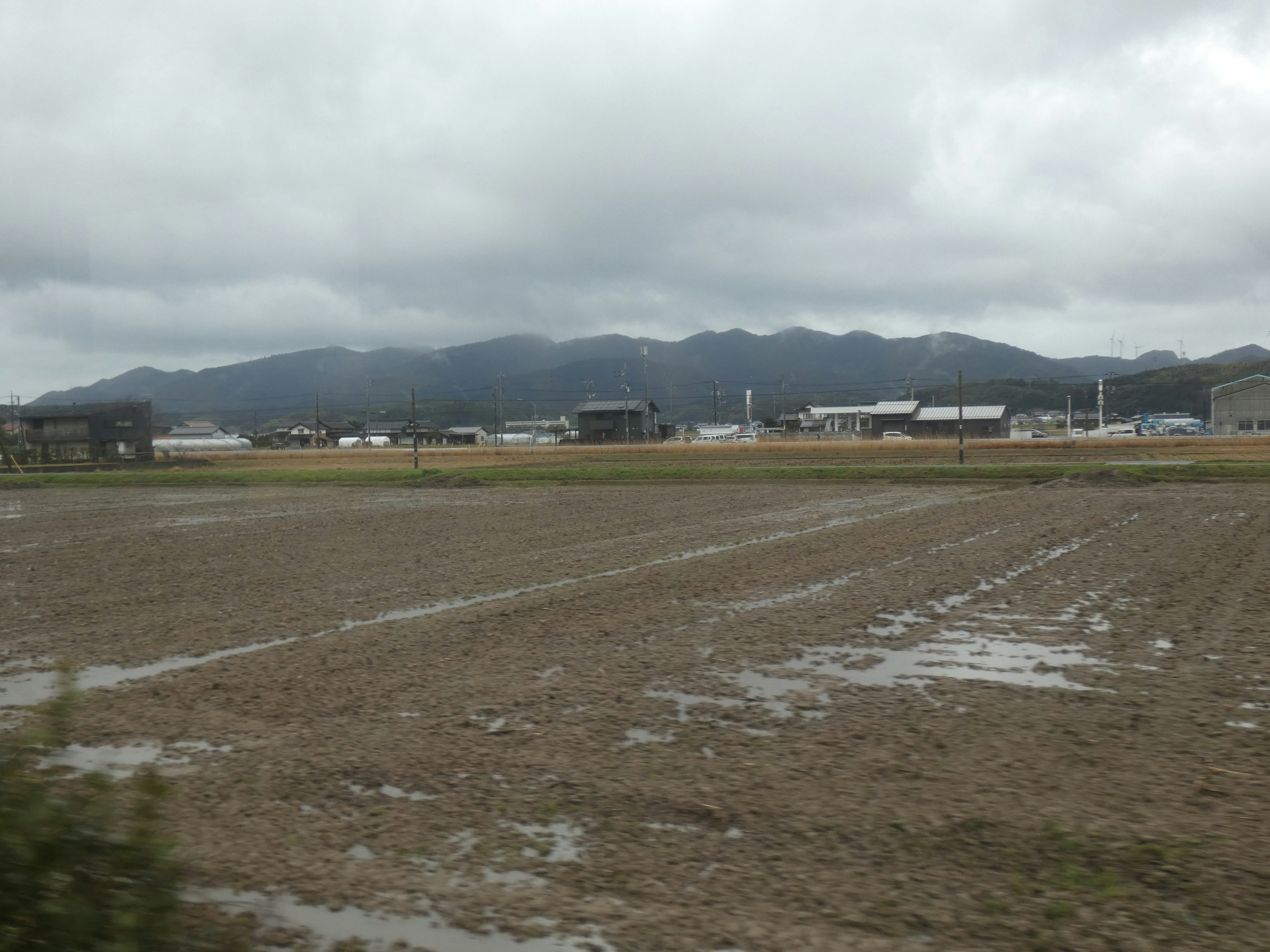 Landscape featuring farmland and mountains cloudy sky with wet soil